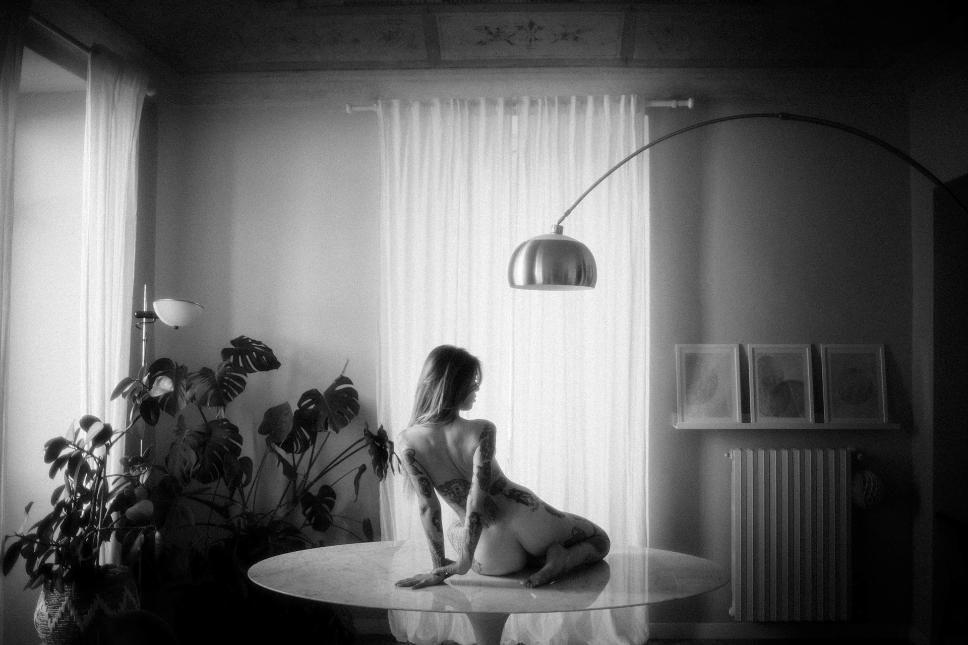 Fine art nude photograph of a woman sitting on a table, seen from behind, in soft natural window light