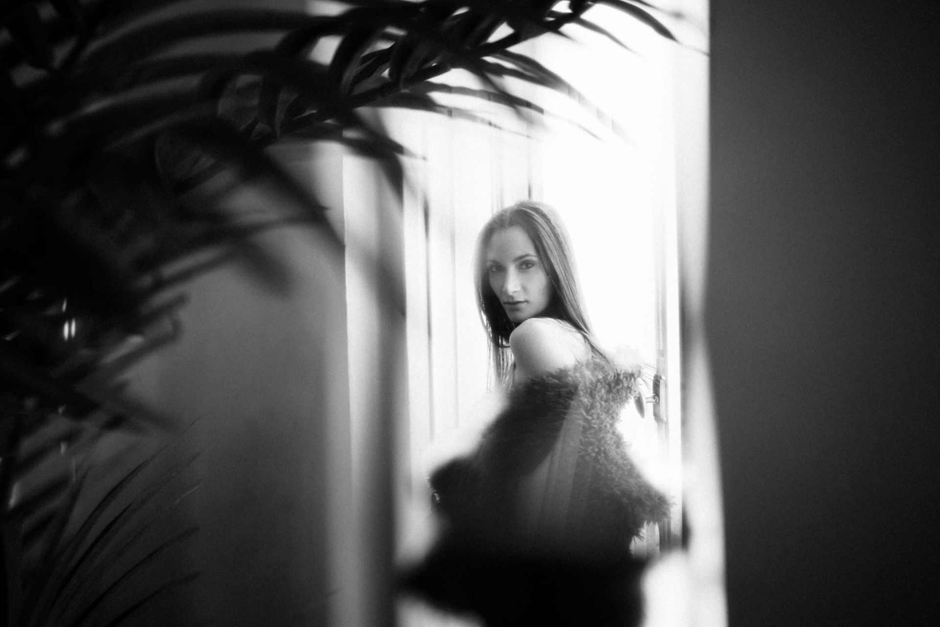 Fine art portrait of a woman wrapped in fur, looking toward the camera in window light