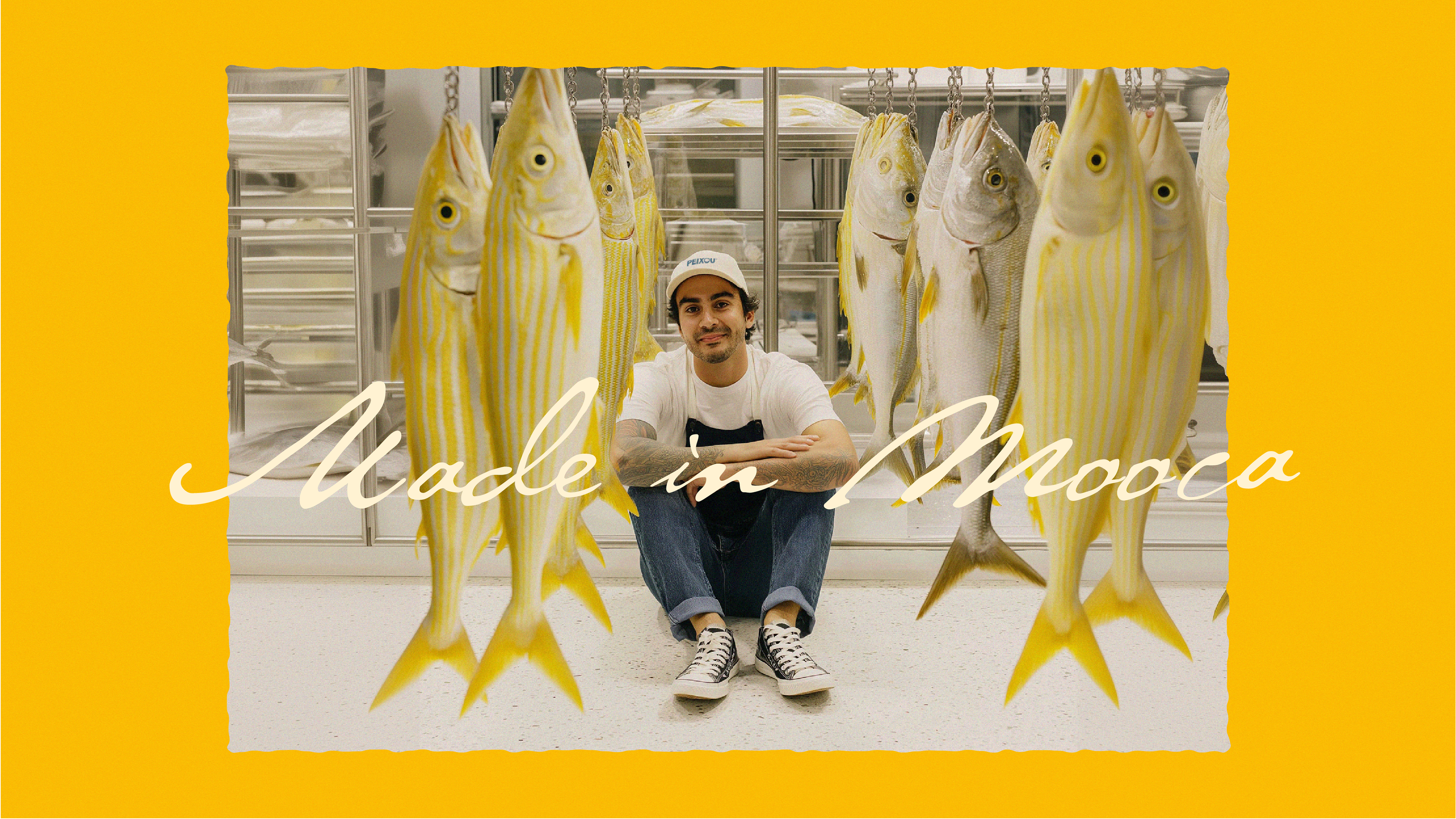Jovem entre peixes pendurados com a frase “Made in Mooca”, reforçando a origem local da Peixou.