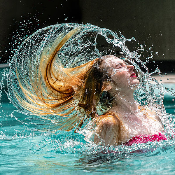 Dramatic lifestyle photo of a female model flipping her hair in a swimming pool, creating a splash effect