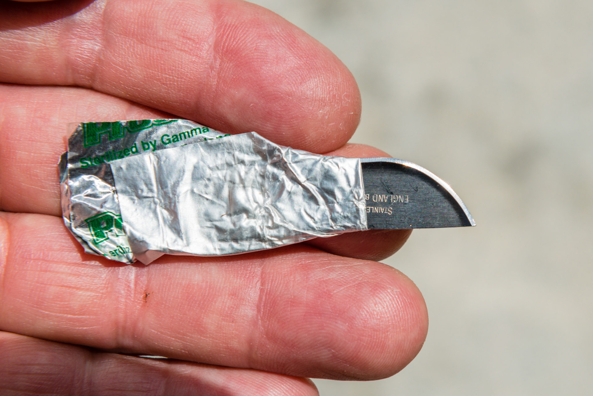 A #22 surgical blade that has been turned around and the dull end reinserted into the foil wrapper and the edges folded around the blade to make a handle.