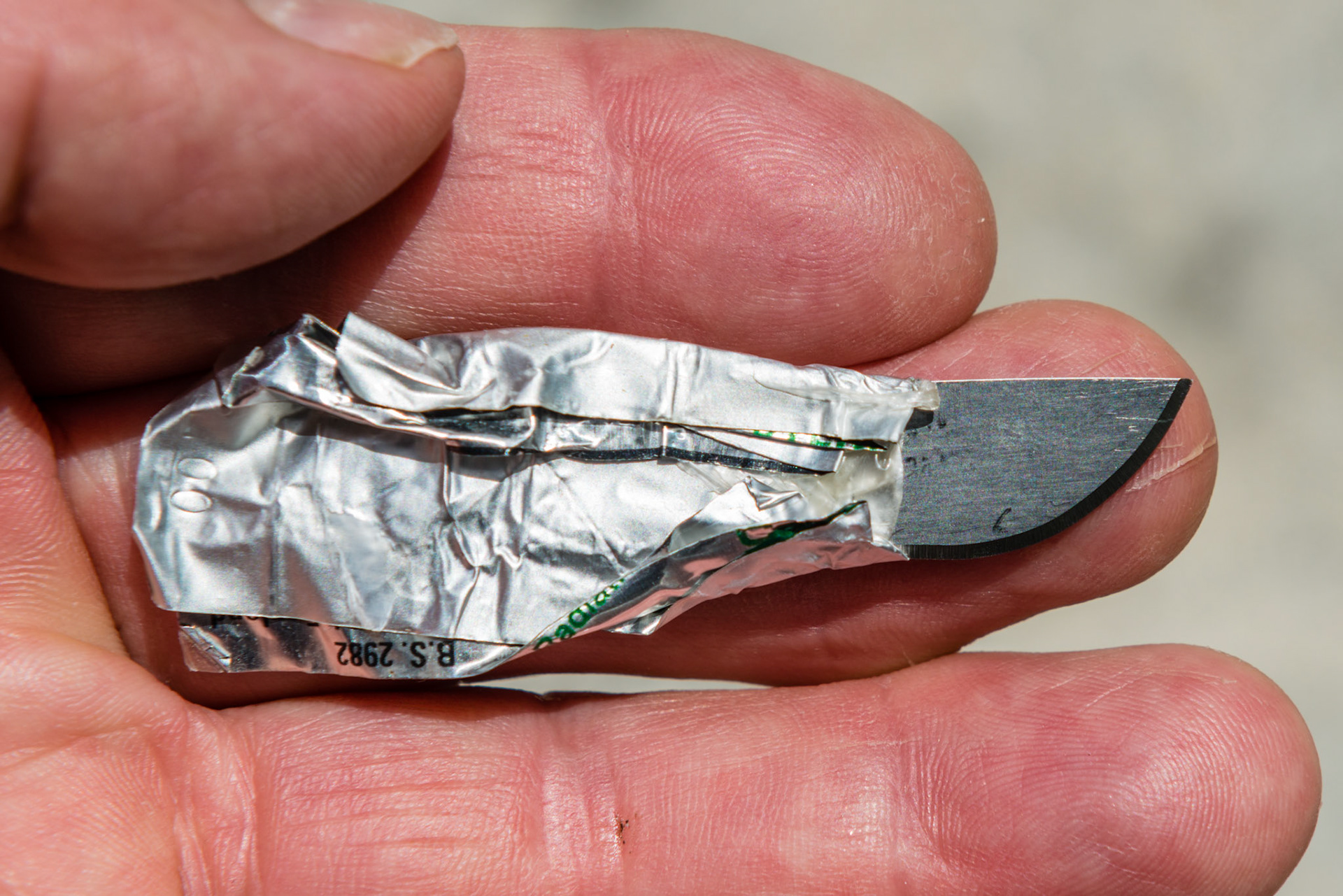 A #22 surgical blade that has been turned around and the dull end reinserted into the foil wrapper and the edges folded around the blade to make a handle.