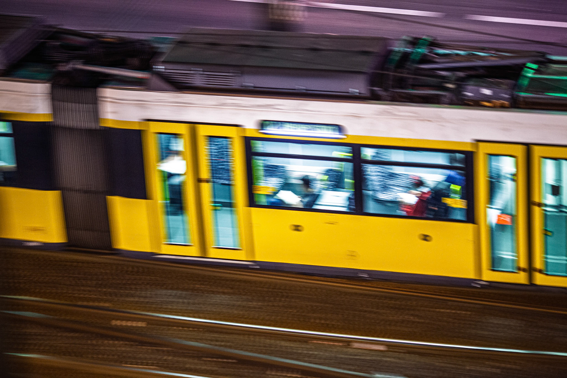 A yellow tram moves smoothly through the lively streets of Berlin at night. City lights illuminate the scene, showcasing passengers inside.