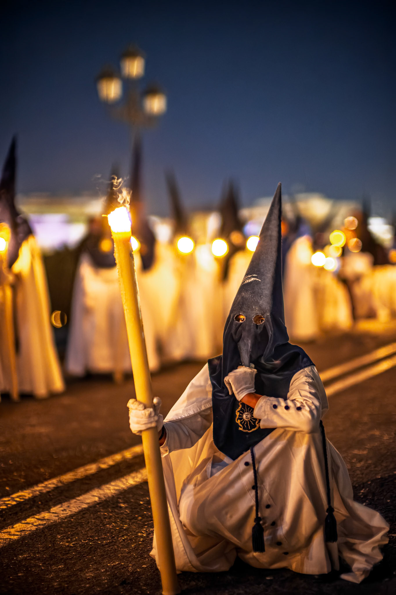 A Nazareno from La Estrella brotherhood rests, squatting with a lit candle, at the end of the Palm Sunday procession in Seville during Holy Week.
