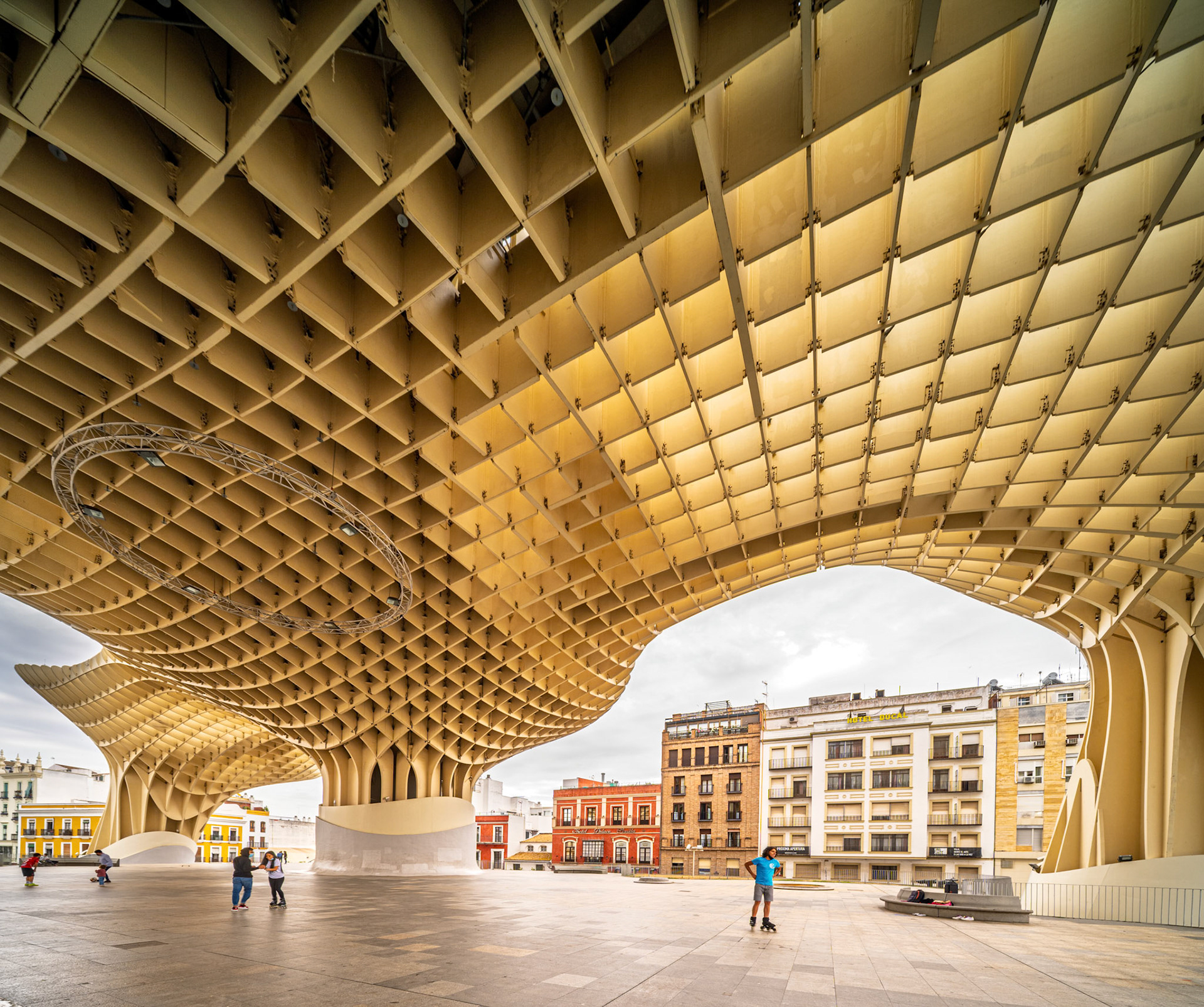 Visitors stroll beneath the unique undulating canopy of Metropol Parasol in Seville, enjoying shaded walkways amid historic architecture and modern life.