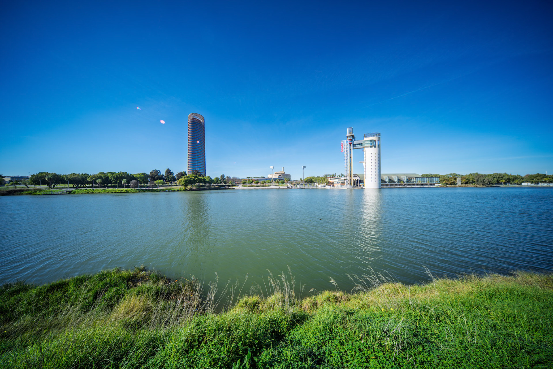 Gaze at the dynamic skyline of Seville, featuring Torre Sevilla and the angular Torre Schindler near the tranquil Guadalquivir River and greenery.