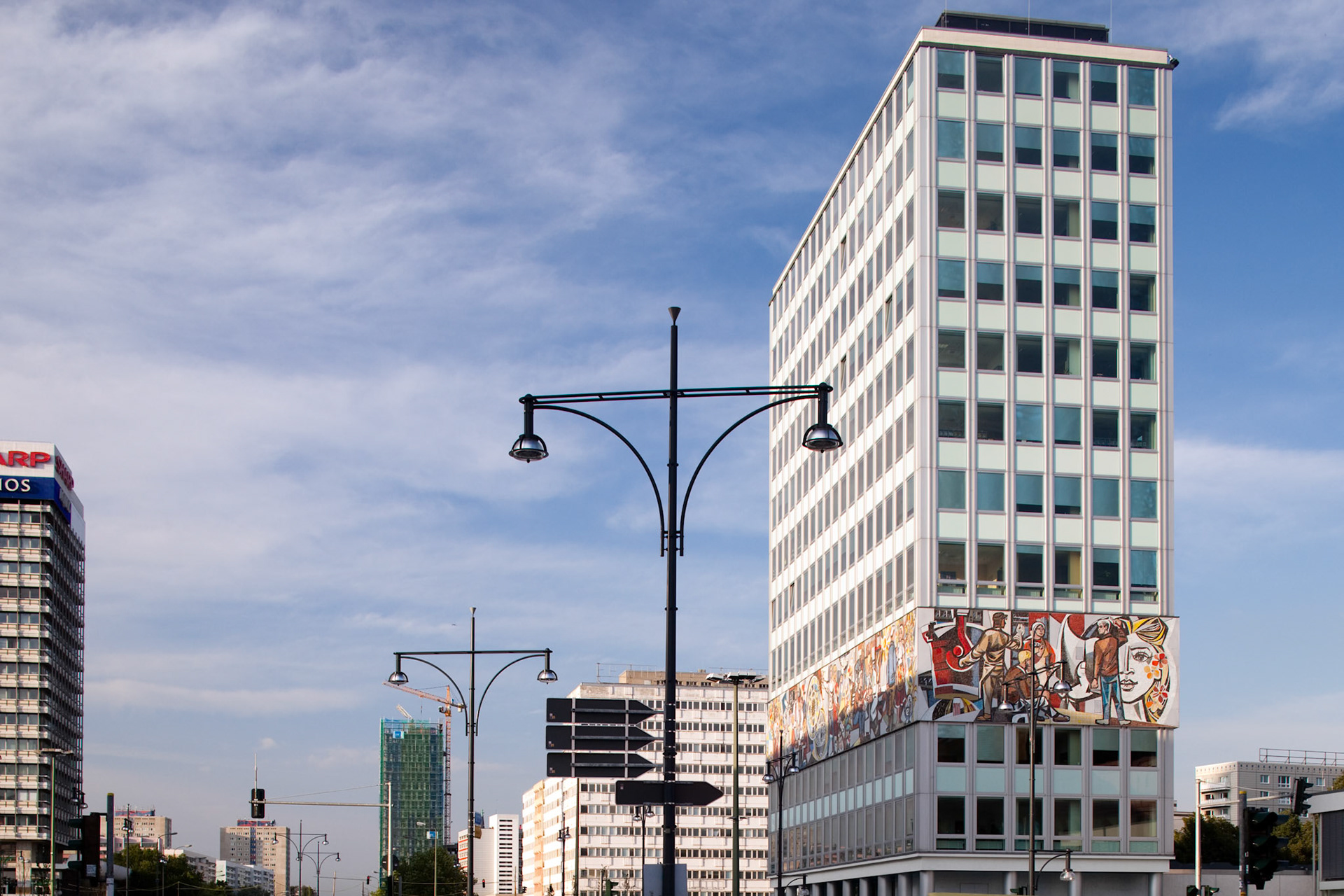 The Haus des Lehrers stands prominently at Alexanderplatz, showcasing a vibrant Socialist mural by Walter Womacka against a blue sky.