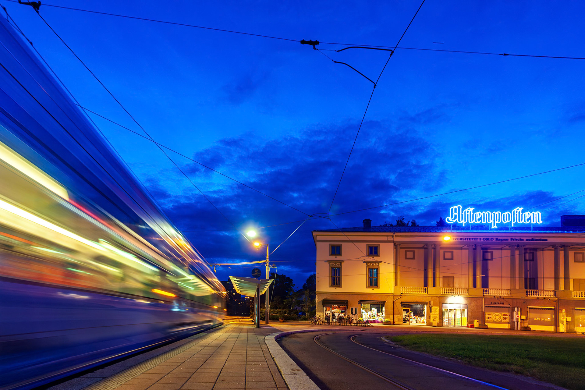 A tram glides past the former Ulleval Kino, now a university auditorium, under a deep blue dusk sky.