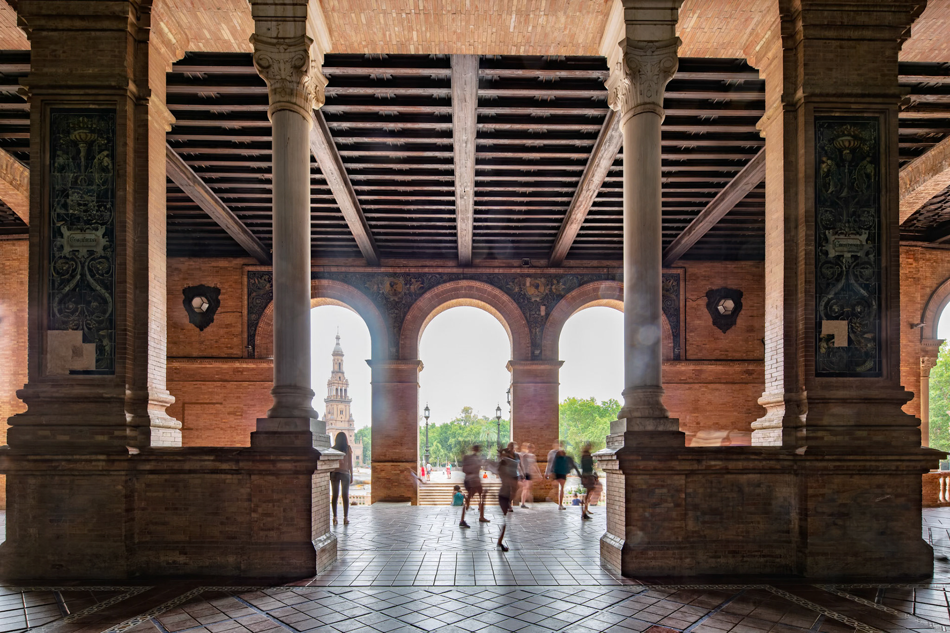 Visitors walk through the iconic arches of Plaza de Espana in Seville, admiring stunning architecture and vibrant scenery during the day.