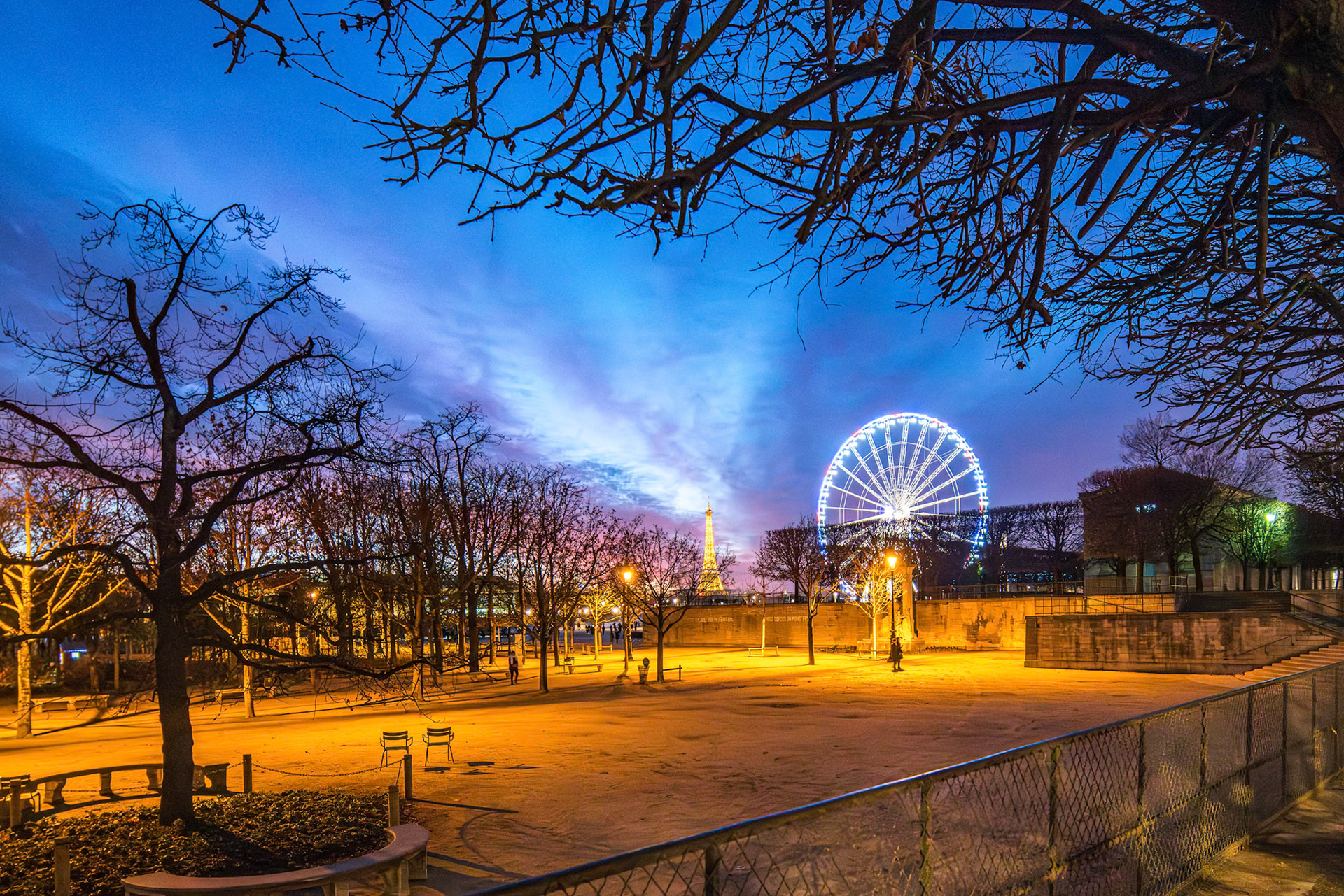 Dusk settles over the Tuileries Gardens, showcasing the radiant Ferris wheel and distant Eiffel Tower.