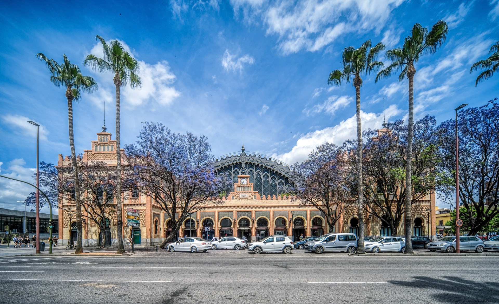 Old train station featuring Neo-Mudéjar architecture surrounded by palm trees and vibrant blooms.