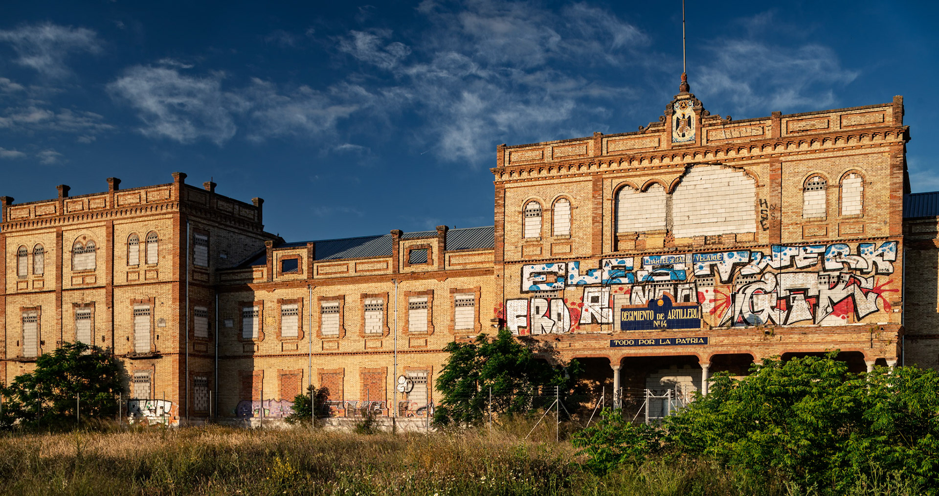 The former Artillery Regiment RACA 14 stands abandoned in Seville, Spain, showcasing striking architecture and vivid graffiti artistry.