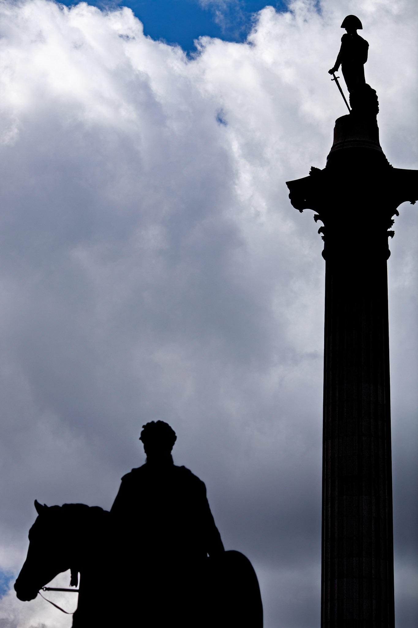 George IV statue stands tall in Trafalgar Square with Nelson's Column behind. Cloudy sky adds depth to the historic scene in London.