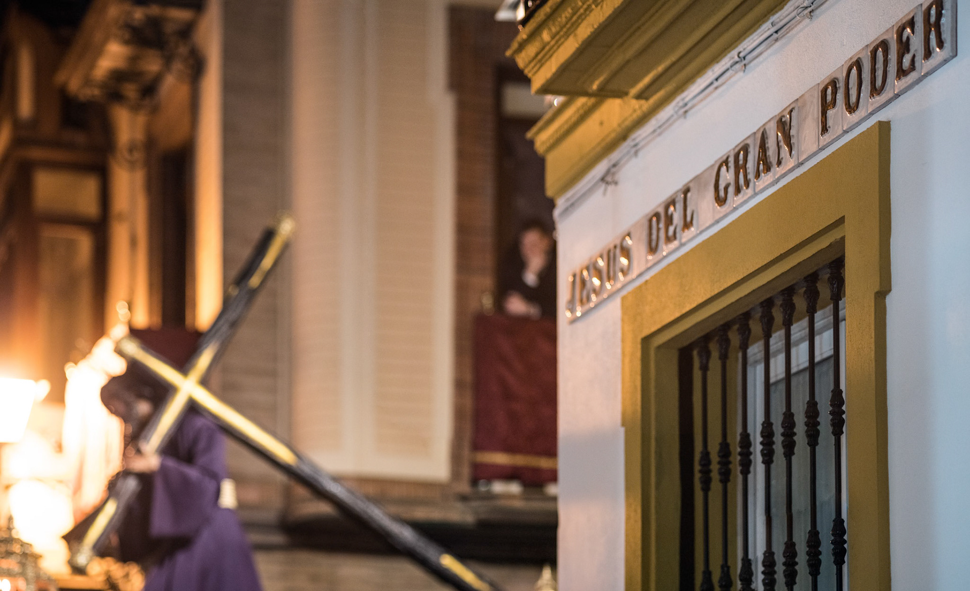 Gran Poder, accompanied by procession members, approaches the street sign during Holy Week in Seville, creating a solemn atmosphere.