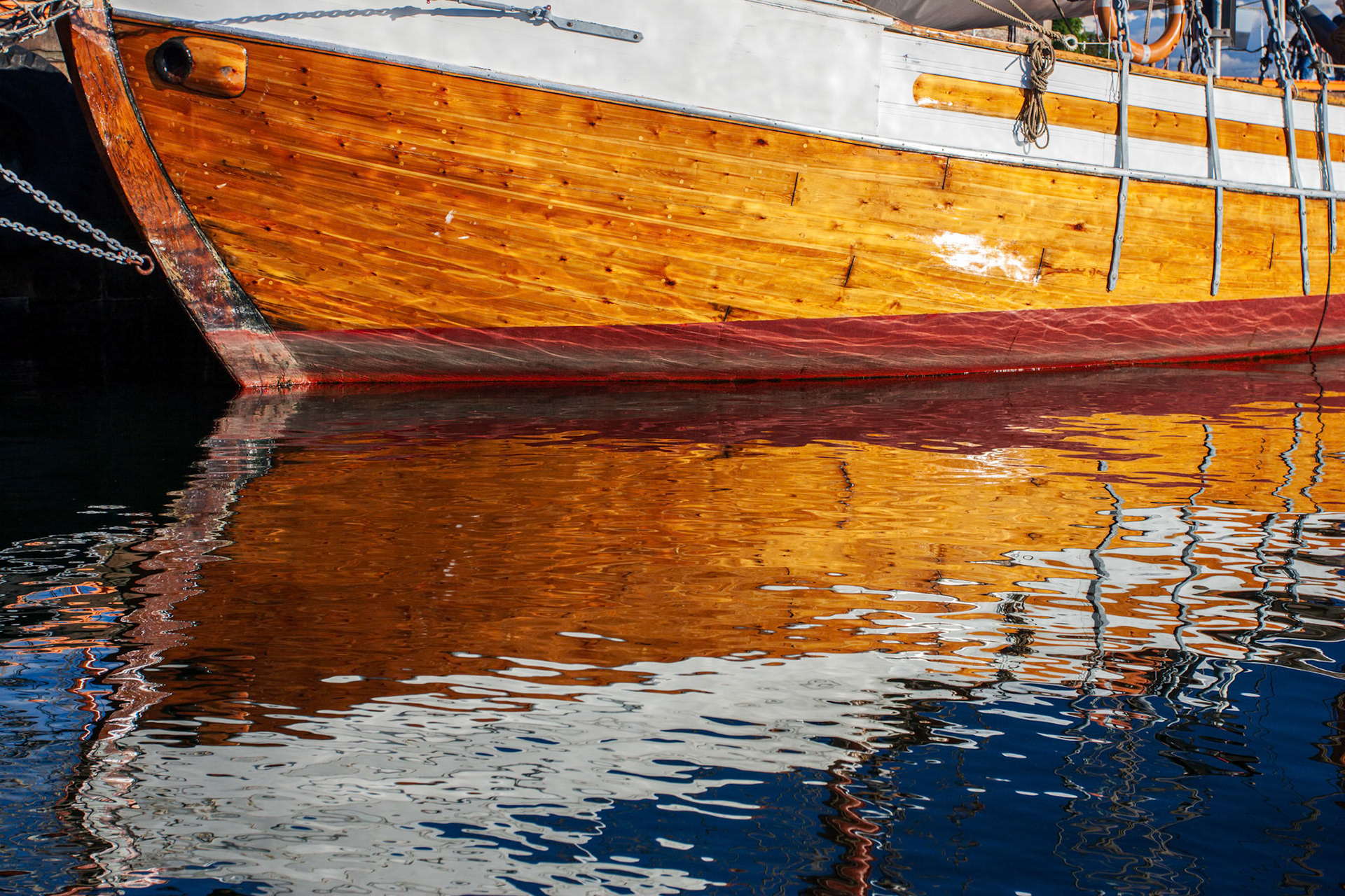A wooden sailing ship is securely moored at Aker Brygge dock, reflecting beautifully on the calm waters of Oslo.