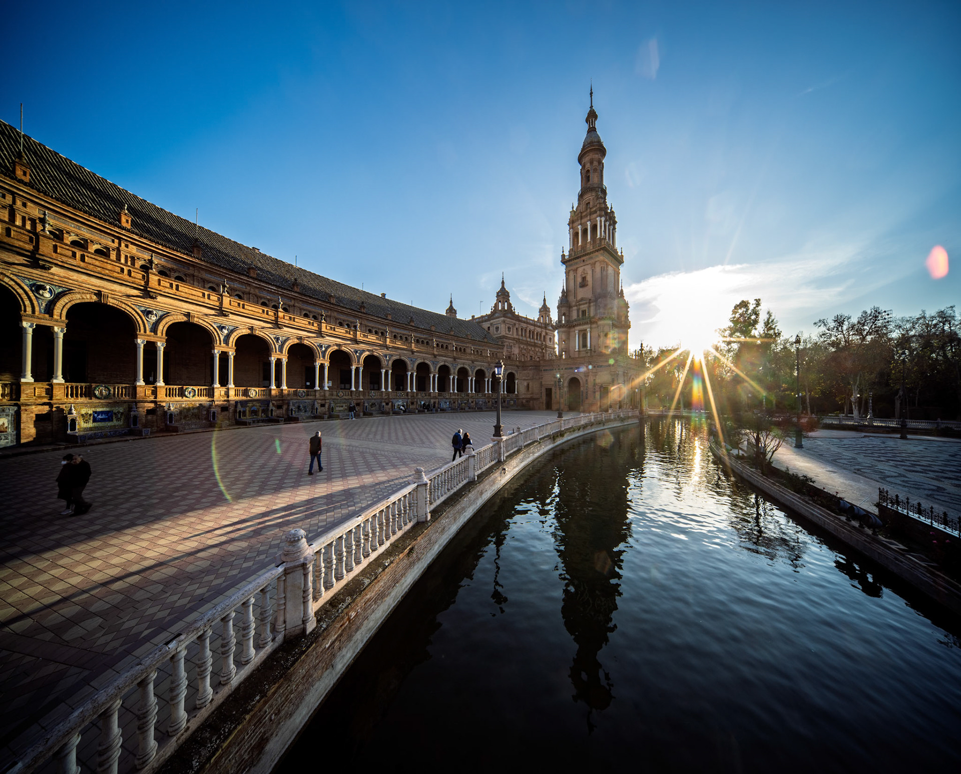 South tower of Plaza de Espana shines golden at sunset, casting reflections on the water as the day ends in Seville, Andalusia, Spain.