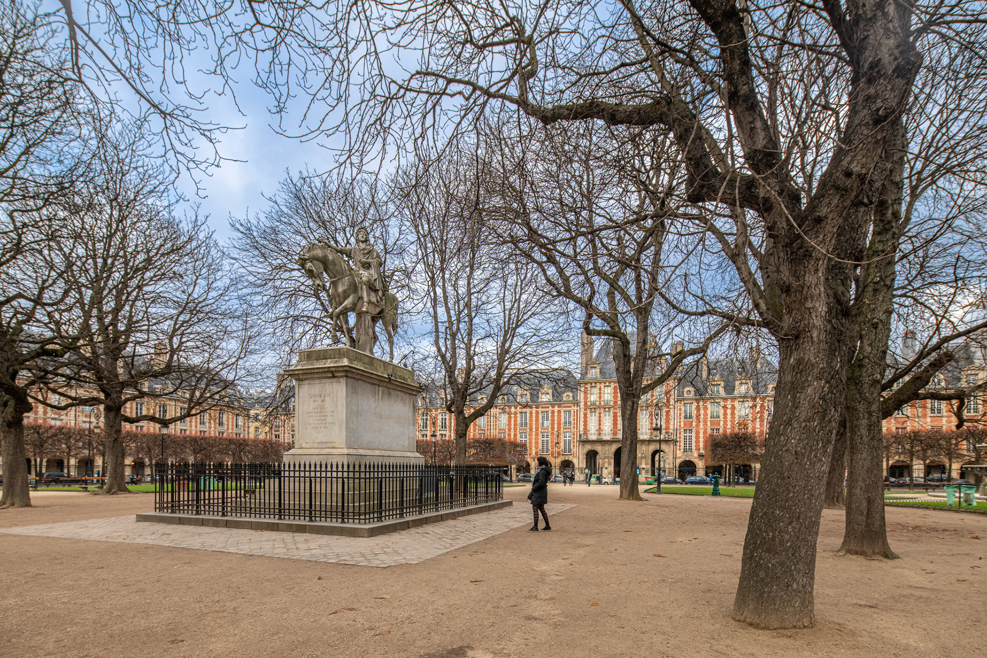 Statue of Luis XIII in Place des Vosges, Paris, France, amidst lush trees.