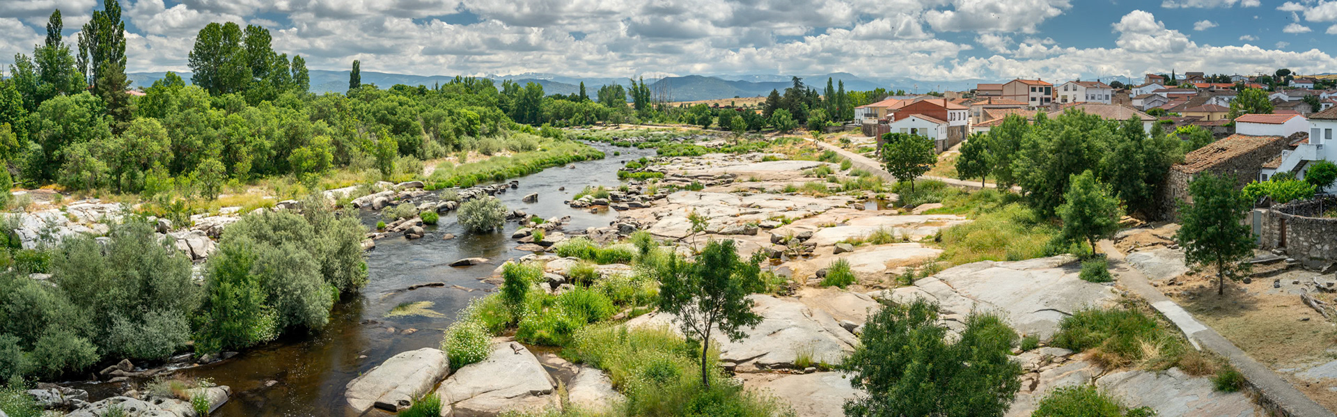 Panoramic view of the Tormes river surrounded by greenery and the town of Puente del Congosto in Salamanca, Spain. Clear skies and tranquil atmosphere.
