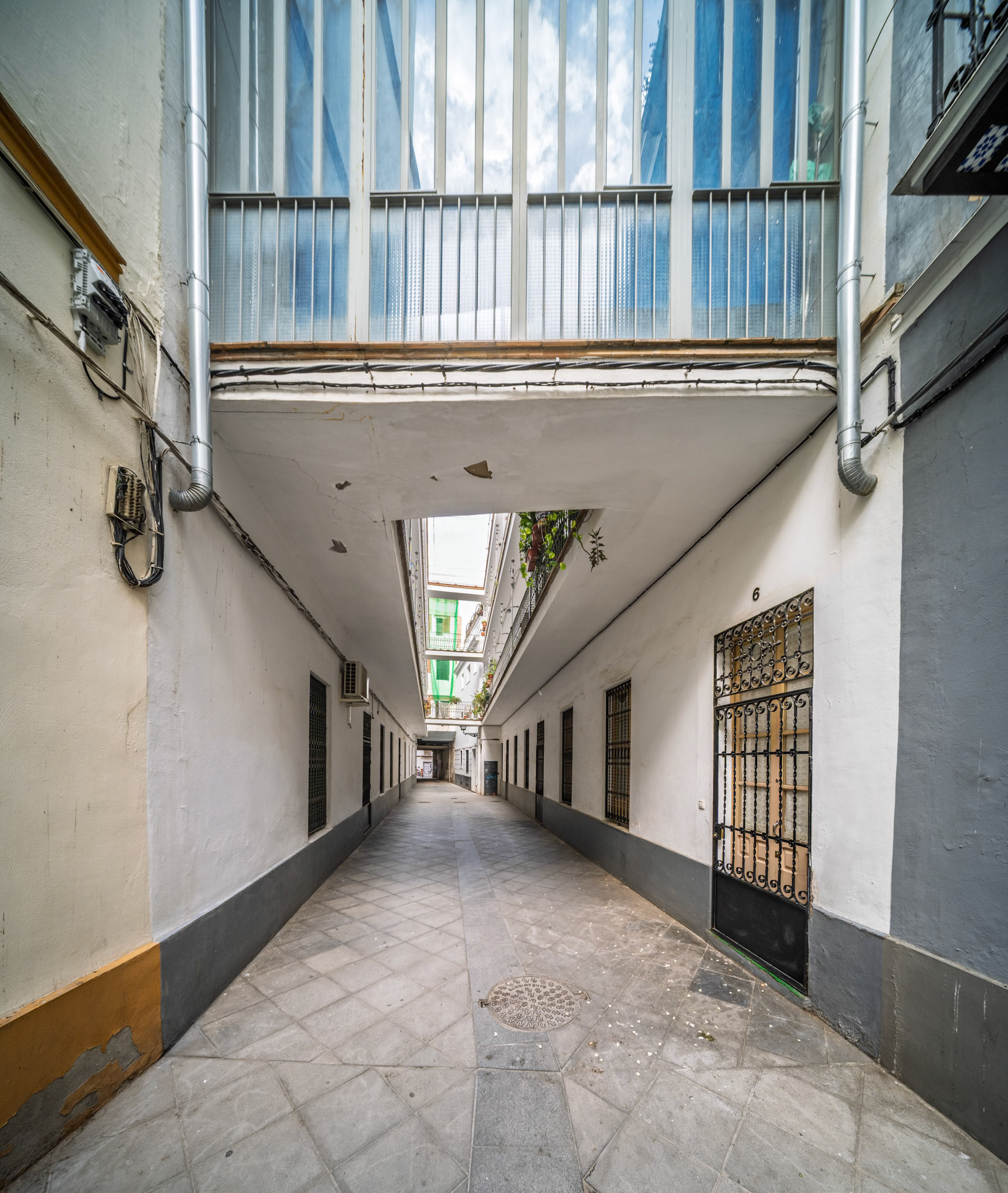 Pasaje Valvanera—social housing corridor designed in 1915 by Manuel Martín, with tiled paving and overhead galleries linking modest dwellings in Seville’s historic core.