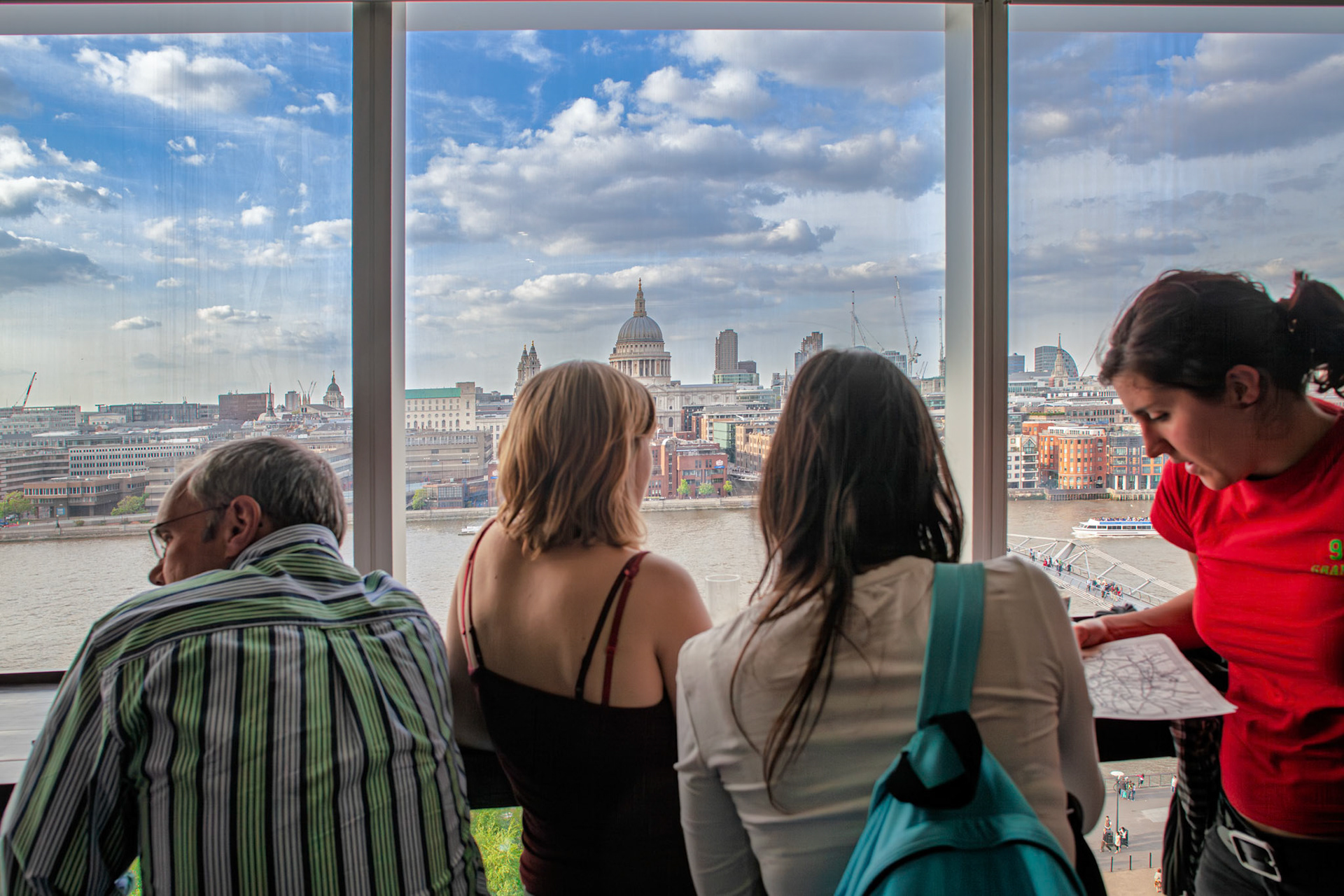Visitors look out at St Pauls Cathedral from the restaurant at Tate Modern Gallery. They observe the city while discussing their plans and experiences.