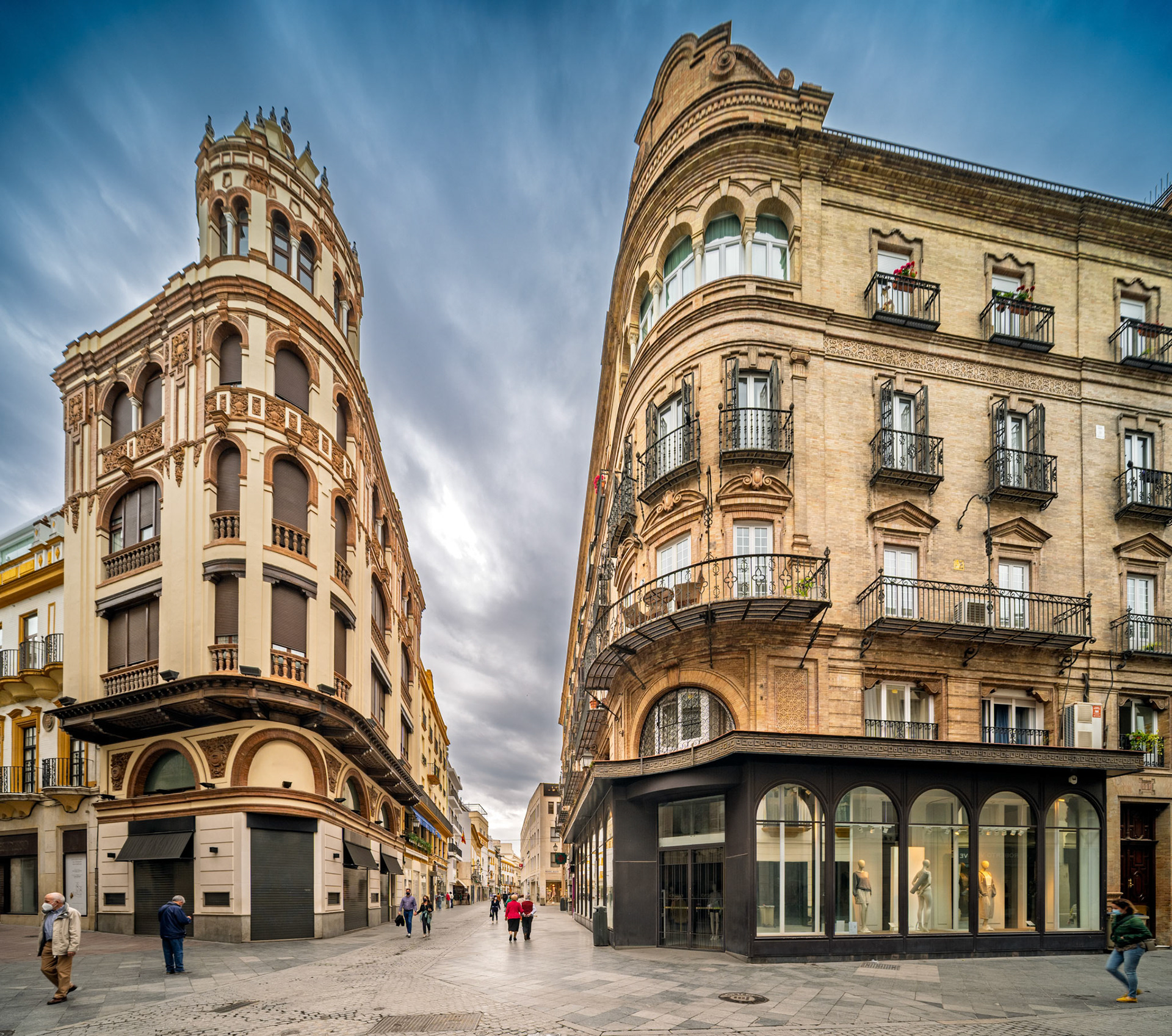 Corner of Tetuán and Rioja in Seville—on the left, the neobaroque Ocaña Carrascosa House (J Talavera Heredia, 1929) rises with its rounded tower. On the right, the Sánchez Dalp House (Aníbal González, 1919) anchors the scene in regionalist elegance