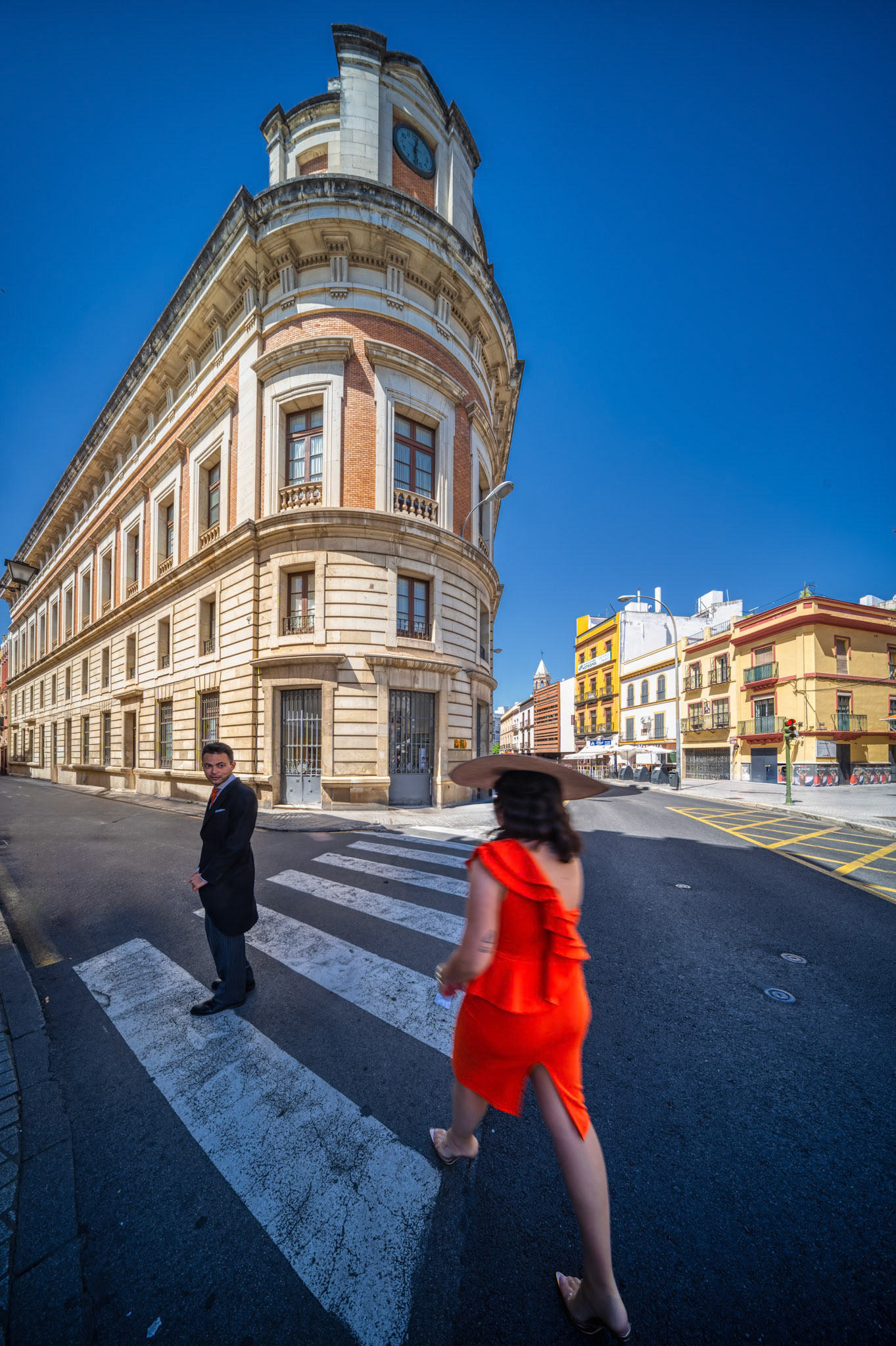 Seville, Spain, May 29 2021, A couple in festive attire crosses the corner of Alhóndiga and Almirante Apodaca, beneath the clocktower of Seville’s former Palace of Justice.