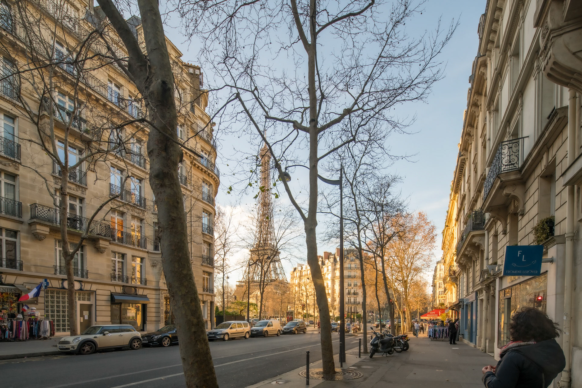 The Eiffel Tower peeks between trees along Avenue de la Bourdonnais at dusk.