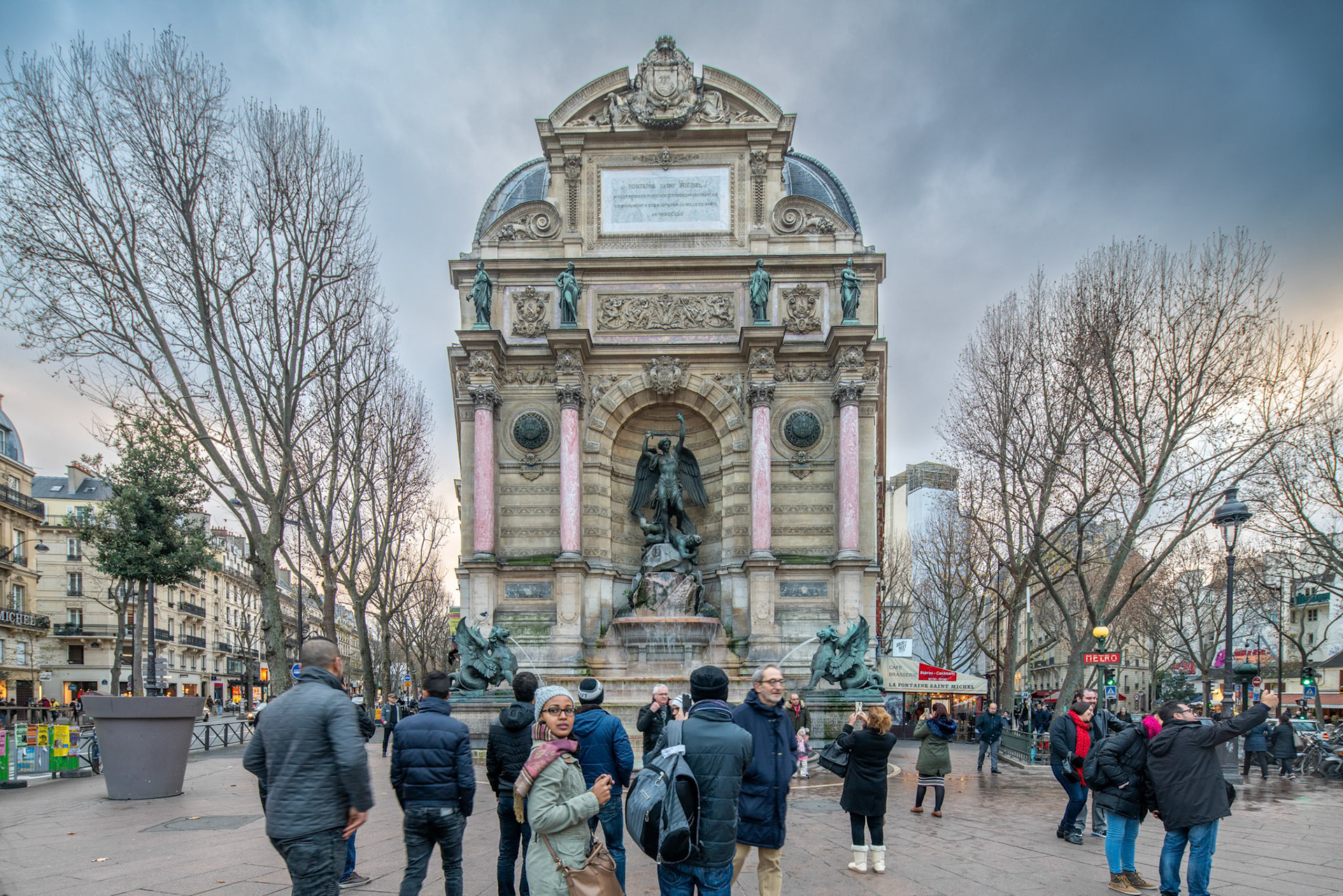 Tourists gather around the iconic Saint Michel Fountain in Paris during the evening.