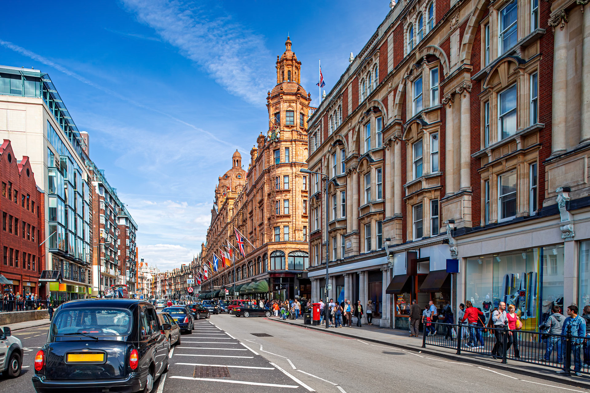 Brompton Road shows busy street life with cars and pedestrians near Harrods building. Flags are visible and buildings line the street under a clear sky.