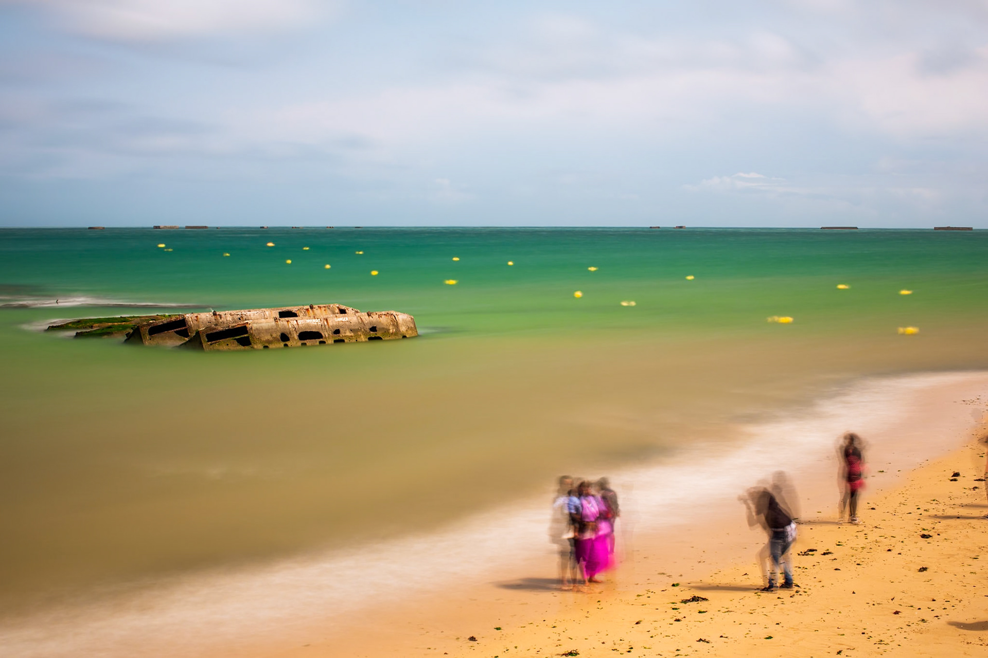 Tourists taking pictures in fronit of the remains of a WW2 Mulberry harbour, Arromanches-les-Bains, Normandy, France