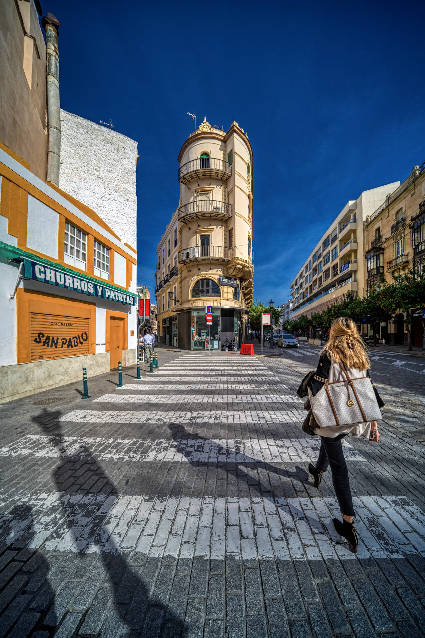 Seville, Spain, Jan 28 2021, A vibrant street scene on Calle San Pablo in Seville, featuring the neobaroque Angel Sanz building by architect Juan Talavera y Heredia, with a passerby walking beneath a clear blue sky.