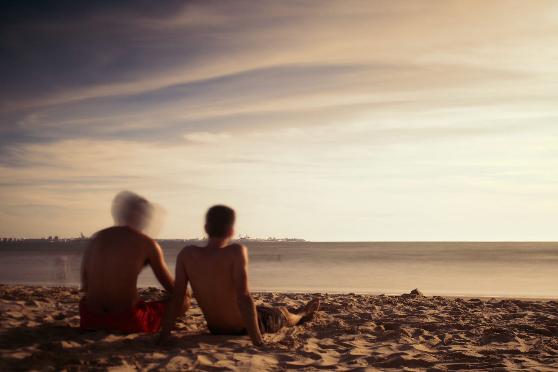 Two boys sitting on the beach and staring at the sea. Daylight long exposure shot by the use of neutral density filters.