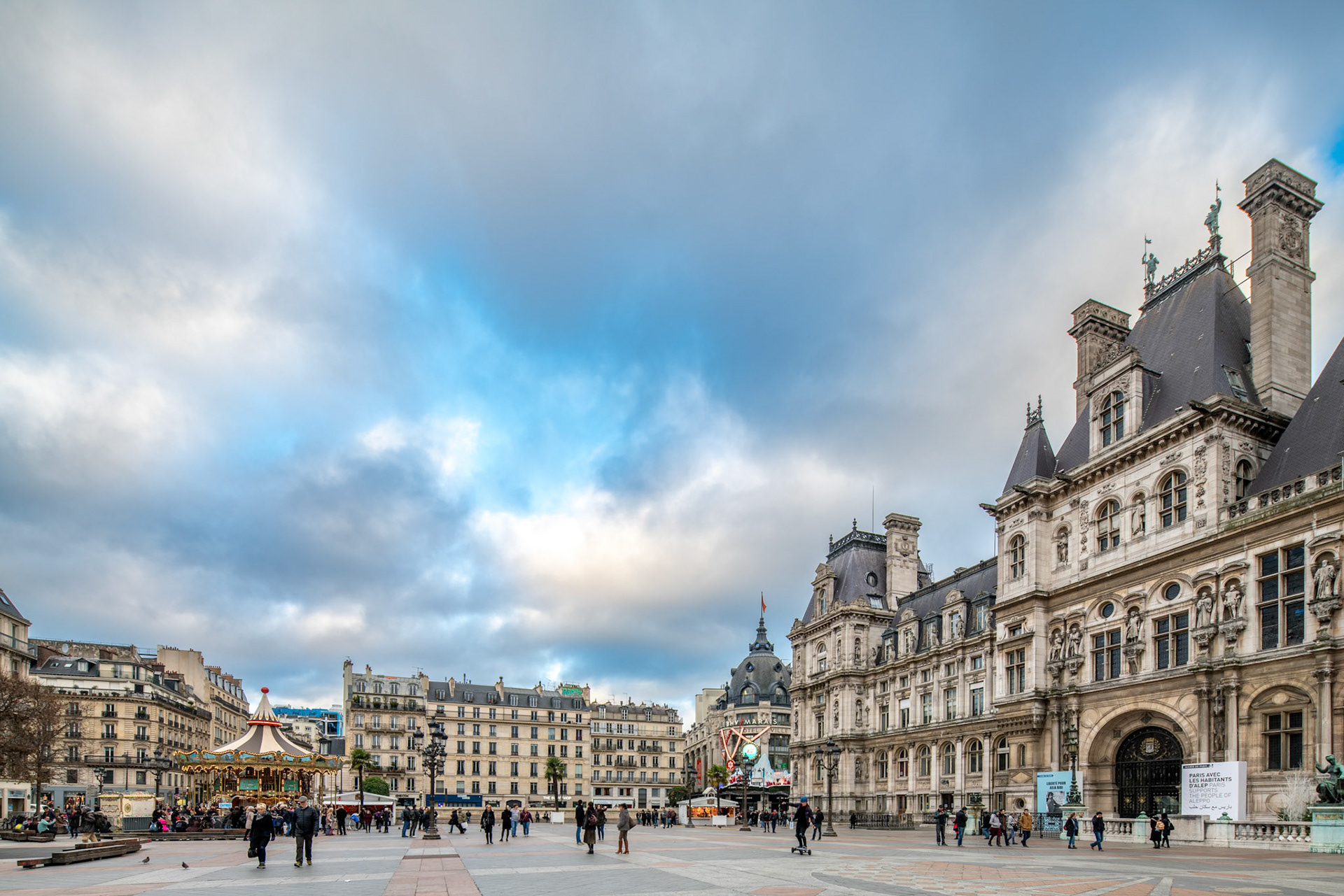 Dusk view of the bustling Hôtel de Ville Square, with pedestrians and the iconic building facade.