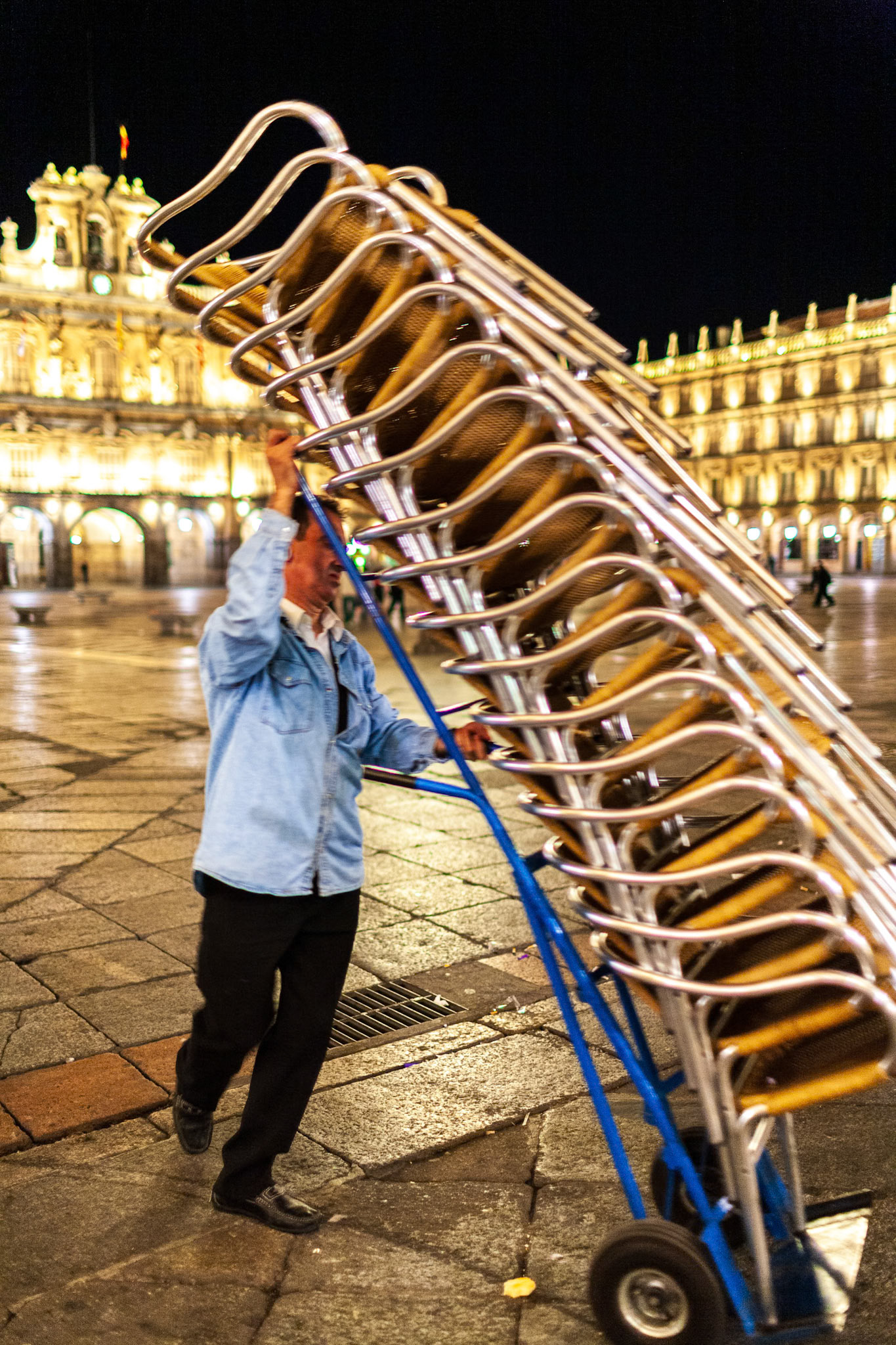 Salamanca, Spain, Aug 18 2018, Worker storing chairs at Plaza Mayor in Salamanca, Spain during nighttime scene.