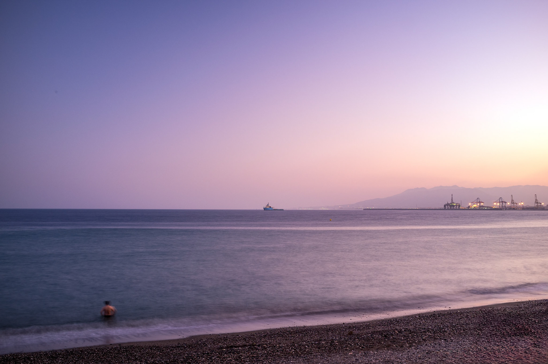 Serene sunset at Playa de los Banos del Carmen beach in Malaga, Andalusia, Spain with views of the distant Malaga port.