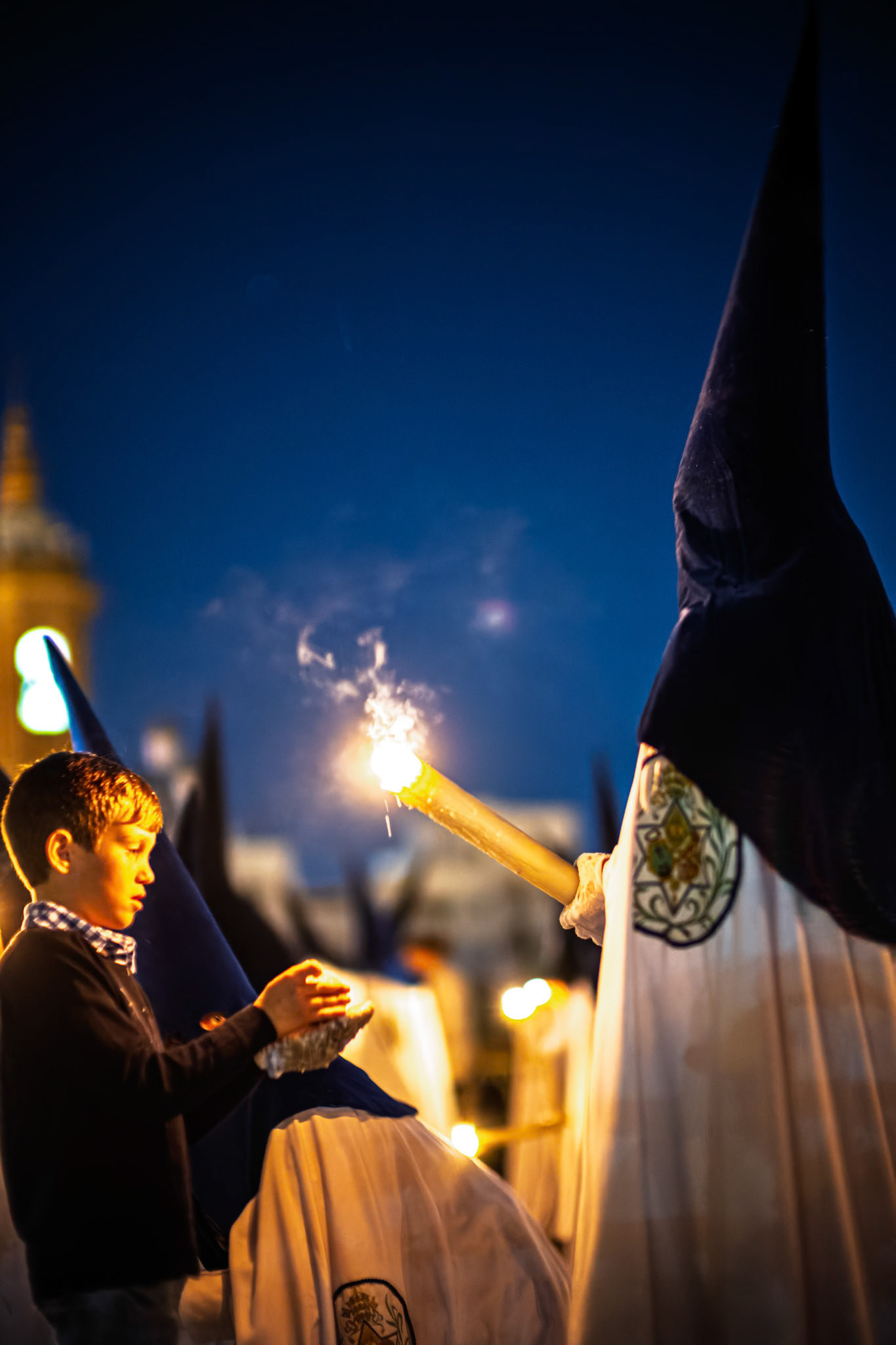 A Nazareno from La Estrella brotherhood pours wax from their candle onto a child's wax ball, a traditional children's custom during Holy Week in Seville, Andalusia, Spain.