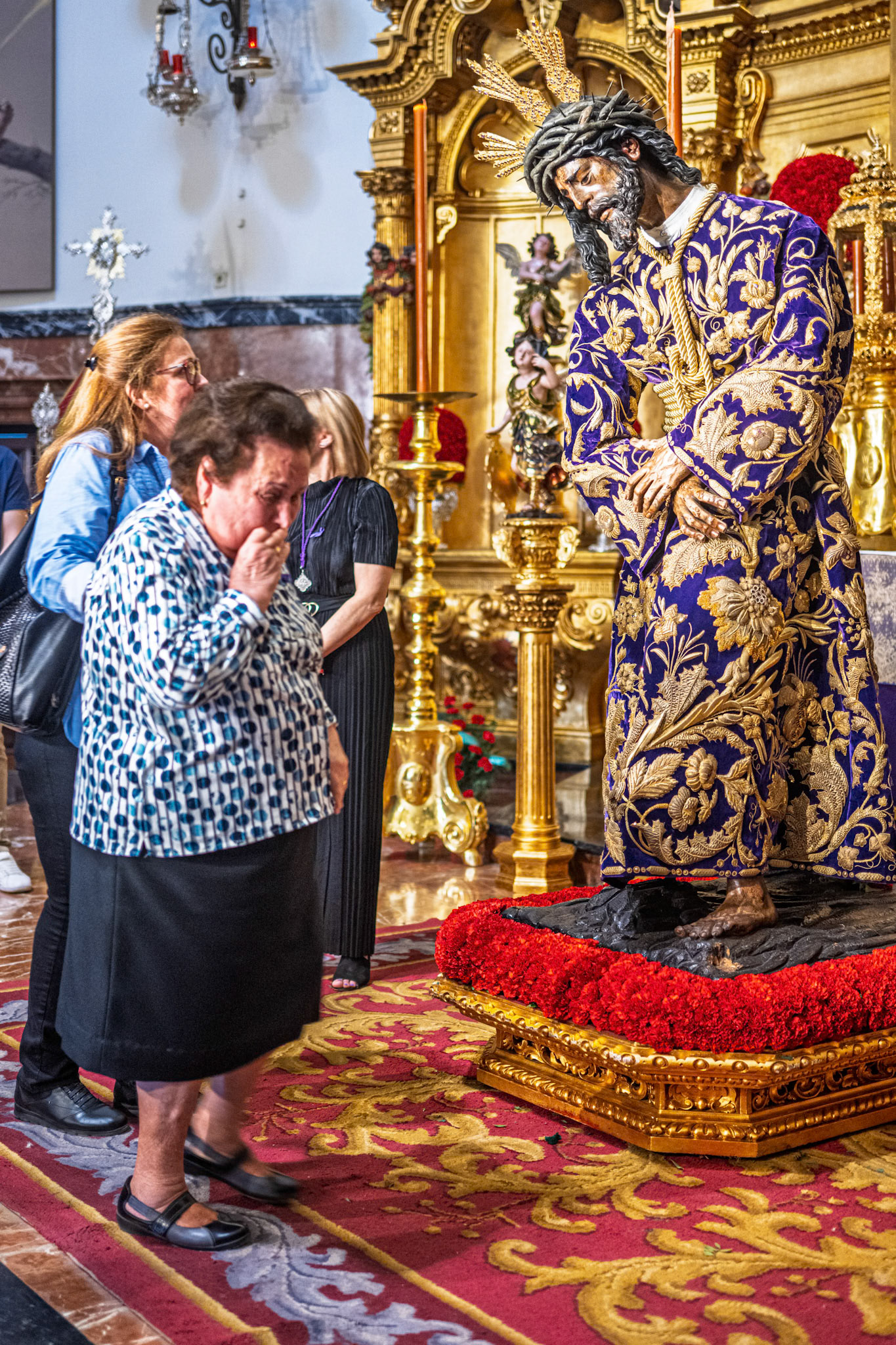 Emotional elderly woman venerates Gran Poder (Great Power) statue, with embroidered tunic, before Good Friday procession in Seville, Spain.