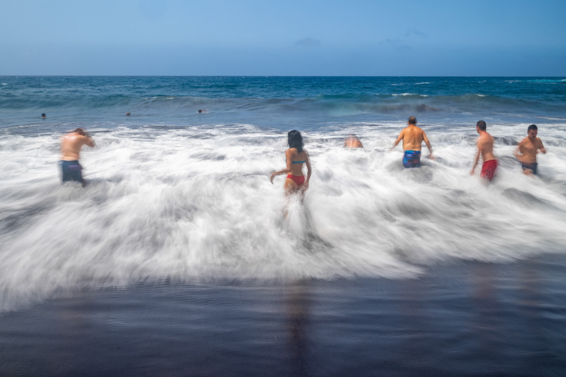 A group of bathers enjoying the waves at Bollullo Beach on the northern coast of Tenerife, La Orotava, Canary Islands, Spain. Long exposure.