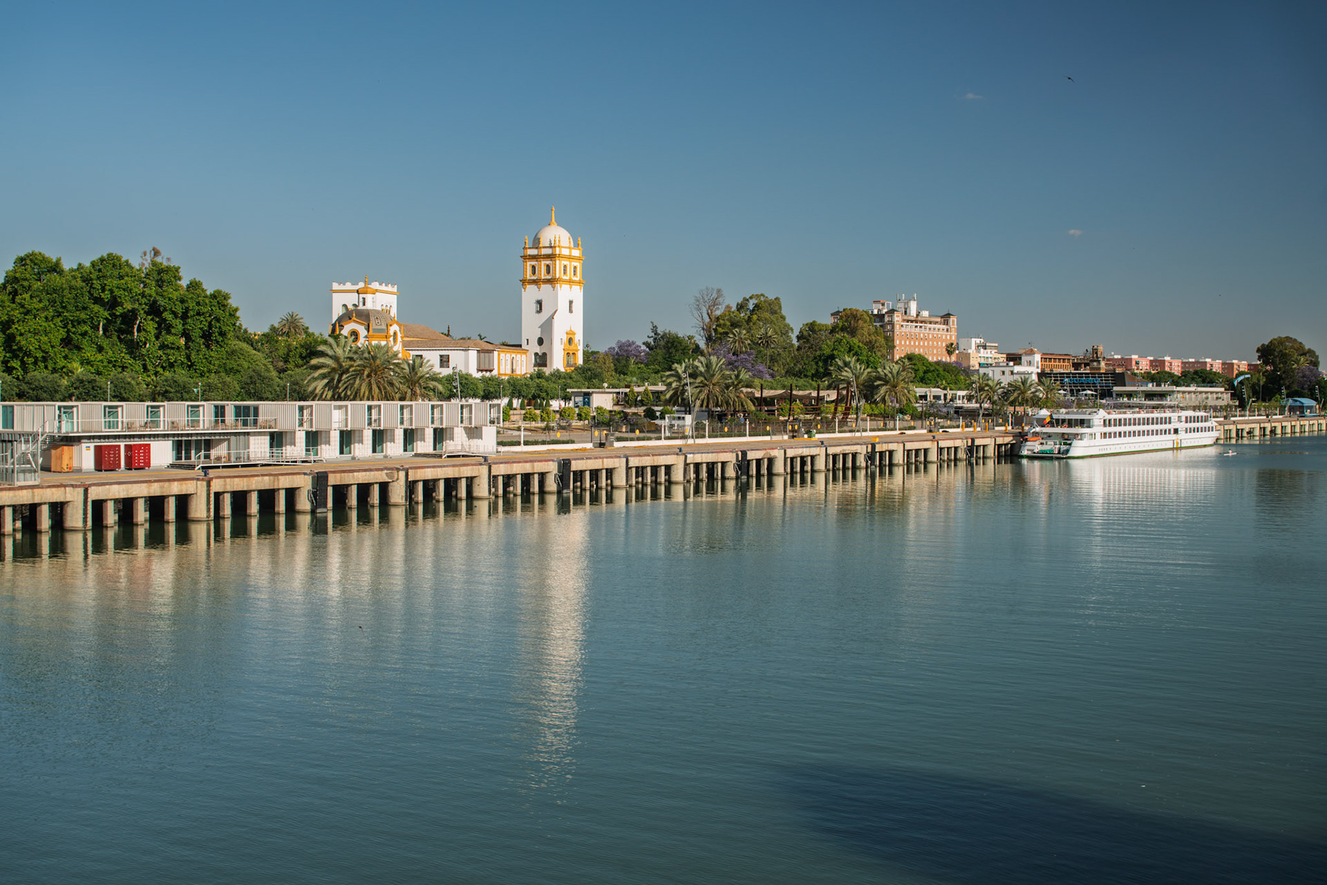 Tourist cruise ship docks at New York Pier beside the Argentina Pavilion, showcasing the beauty of Seville along the Guadalquivir River.