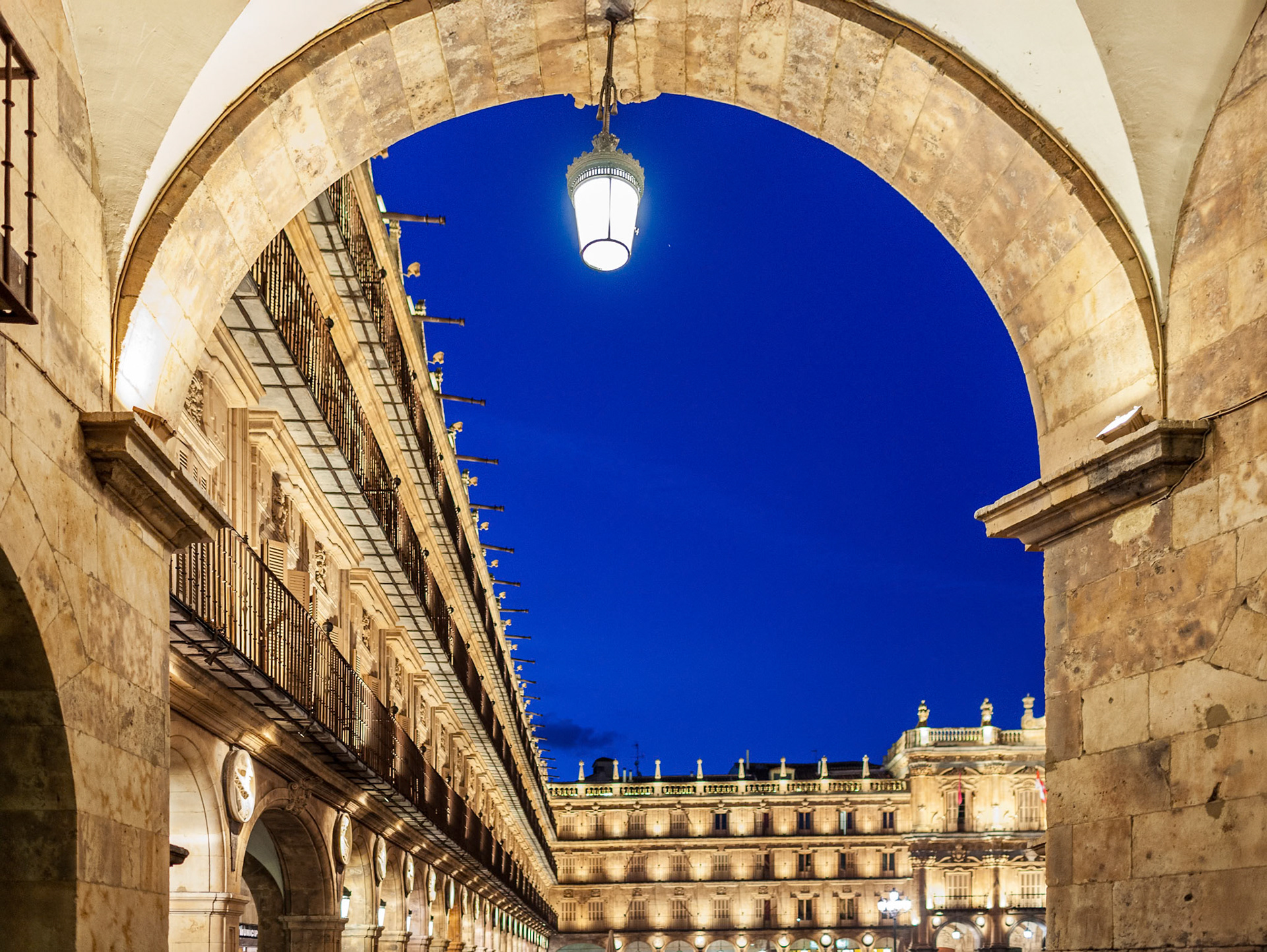 Historic Plaza Mayor in Salamanca, Spain, seen through a lit archway during night.