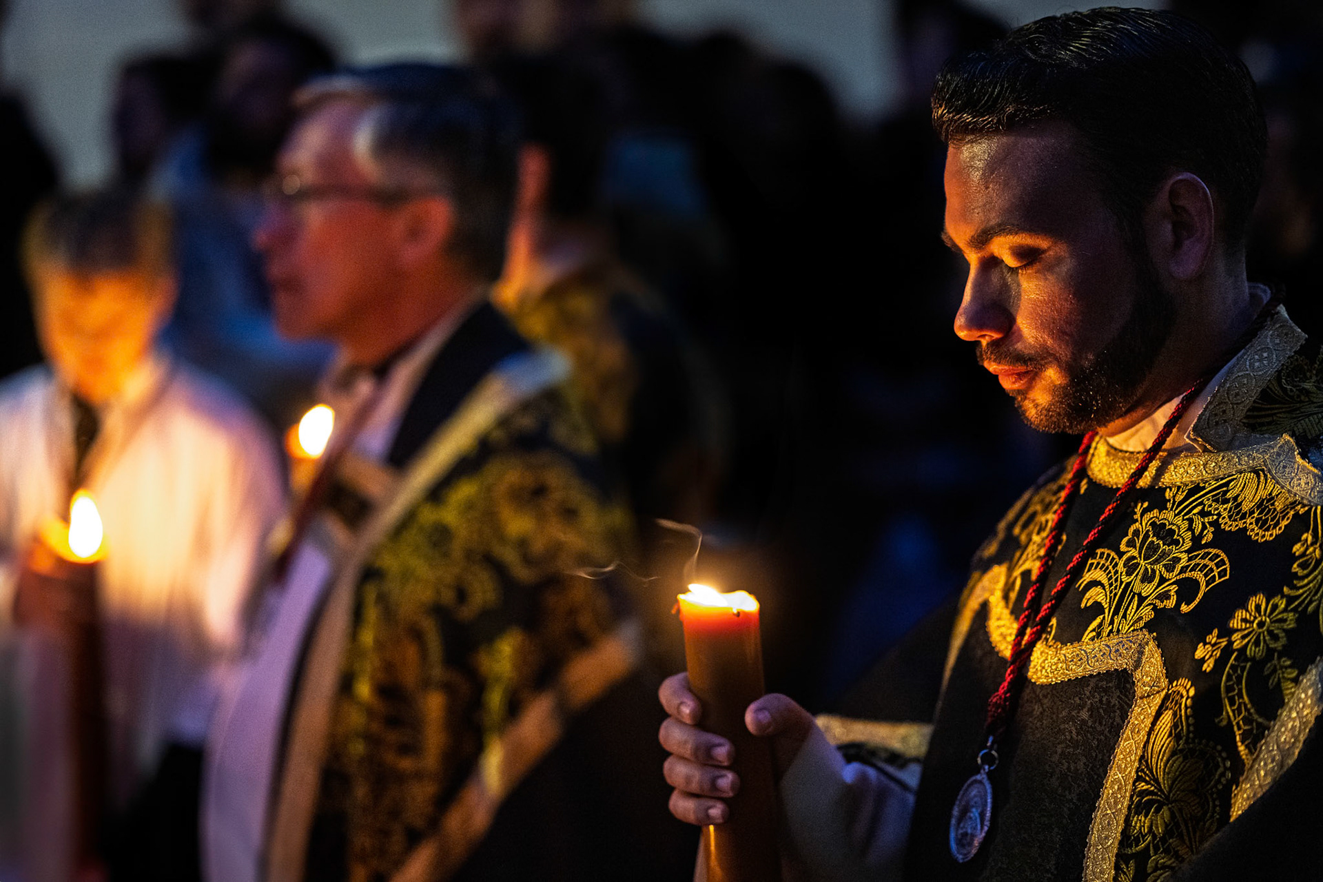 An acolyte in an ornate dalmatic holds a candle, deep in introspection during the Servitas Brotherhood procession on Holy Week in Seville, Andalusia, Spain.