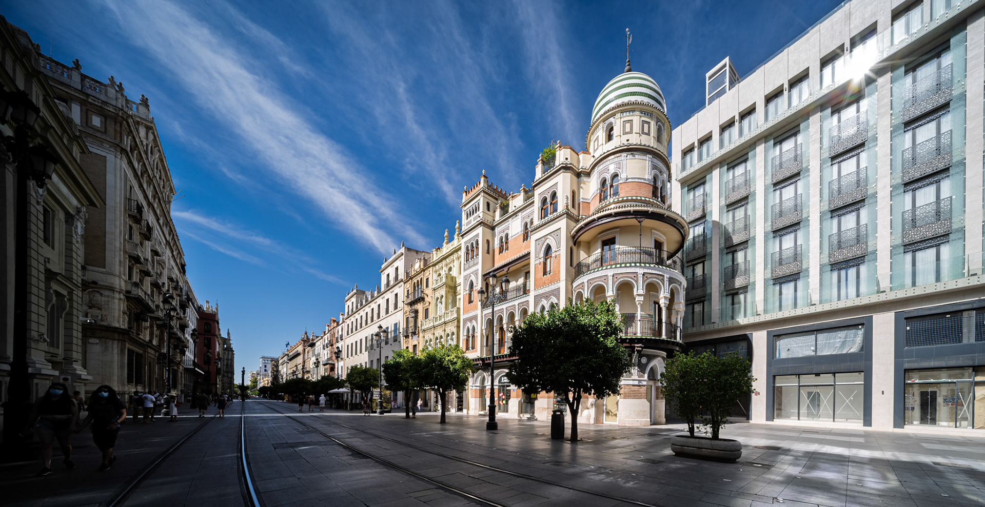 Avenida de la Constitución, Seville—La Adriática building in foreground, its striped dome and ornate façade lit in sharp morning contrast against the clear sky.