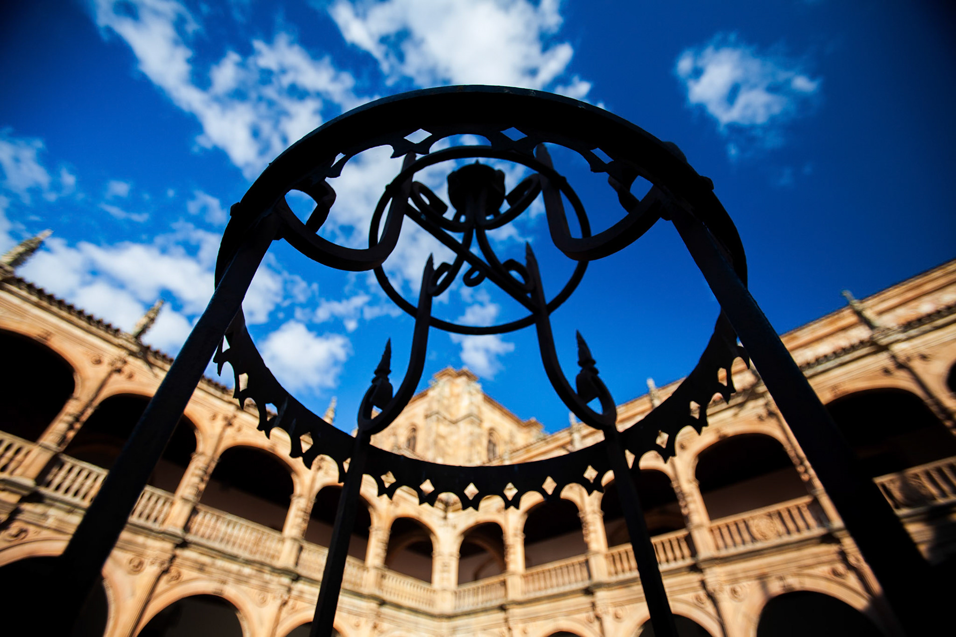 Iron decoration on a well at Fonseca college courtyard under a vibrant blue sky in Salamanca.
