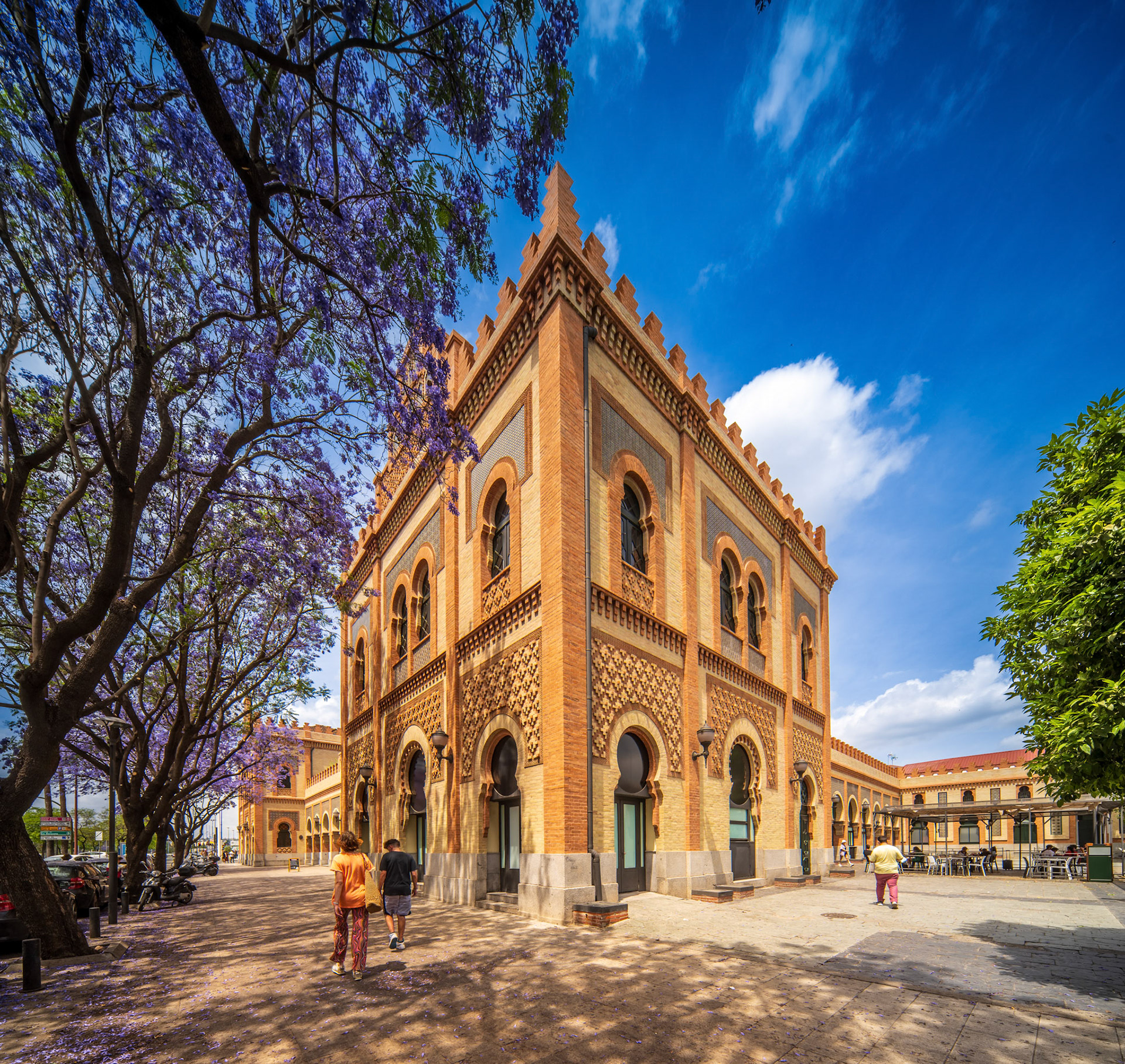 Historic neo-mudejar styled landmark with ornate architecture and blooming jacaranda trees in Seville.
