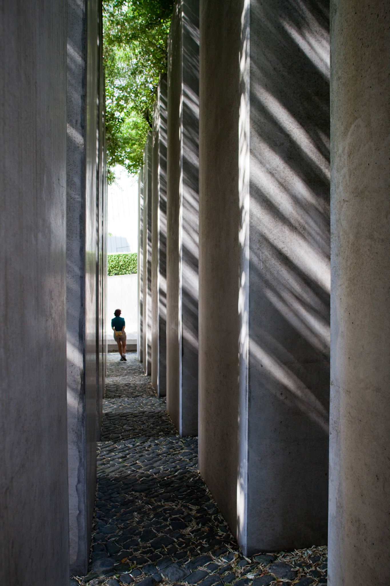Berlin, Germany, July 27 2009, In the Garden of Exile, a visitor walks through tall stone pillars under dappled sunlight, reflecting on history and remembrance.