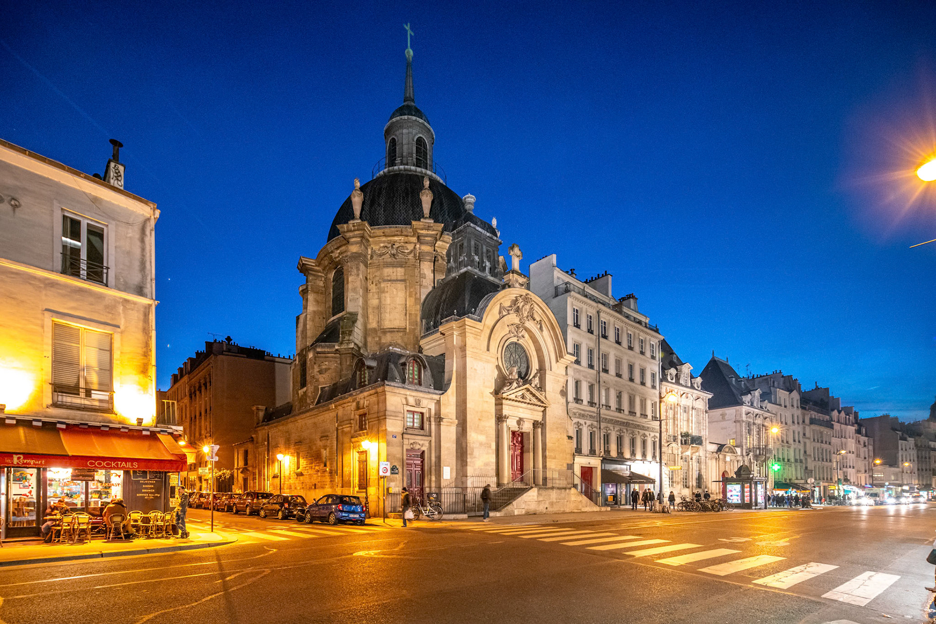 Dusk settles over Eglise Protestante du Marais with city lights illuminating the street.