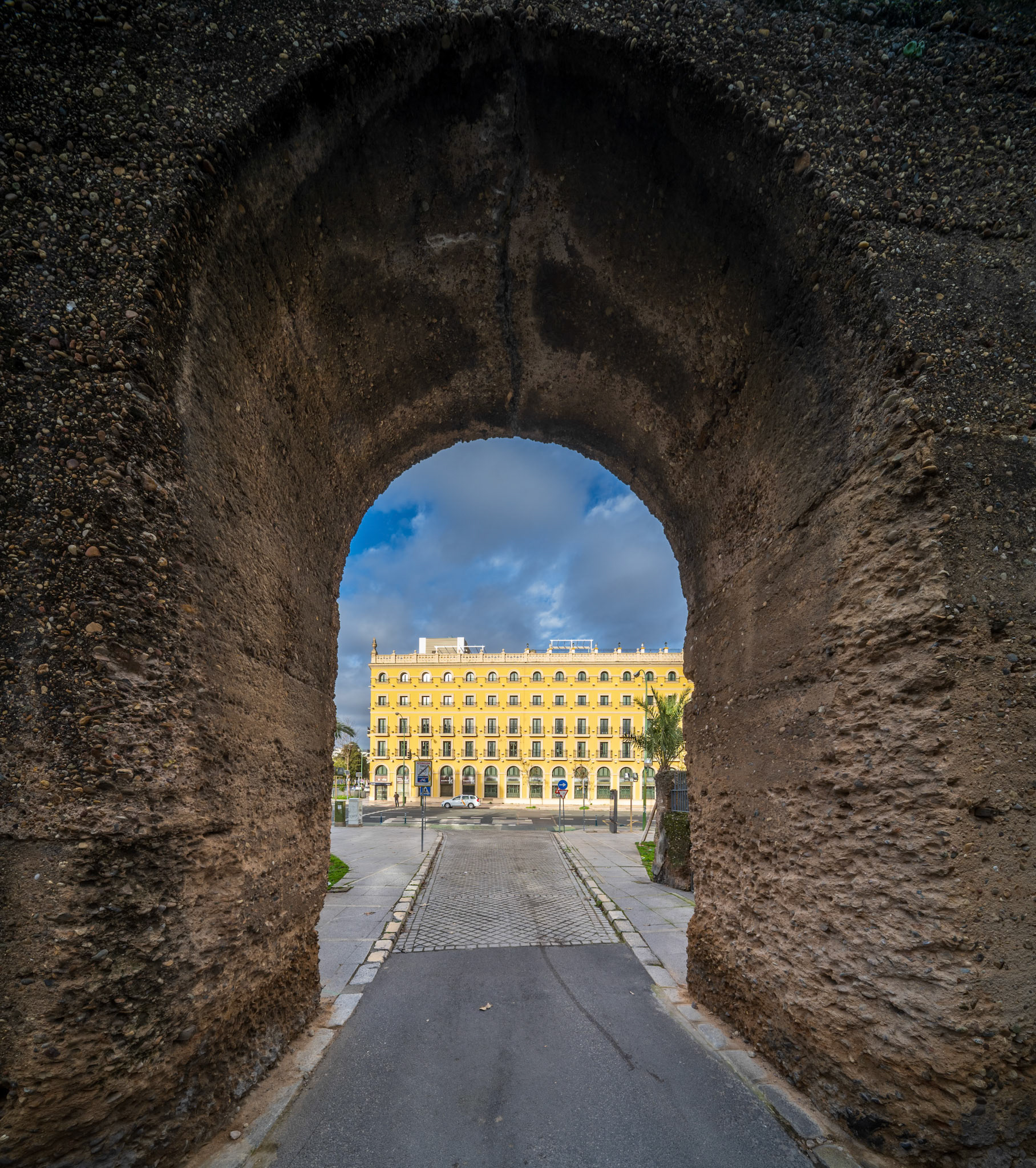 Historic view of Hotel Macarena through ancient wall arch in Seville, Spain.