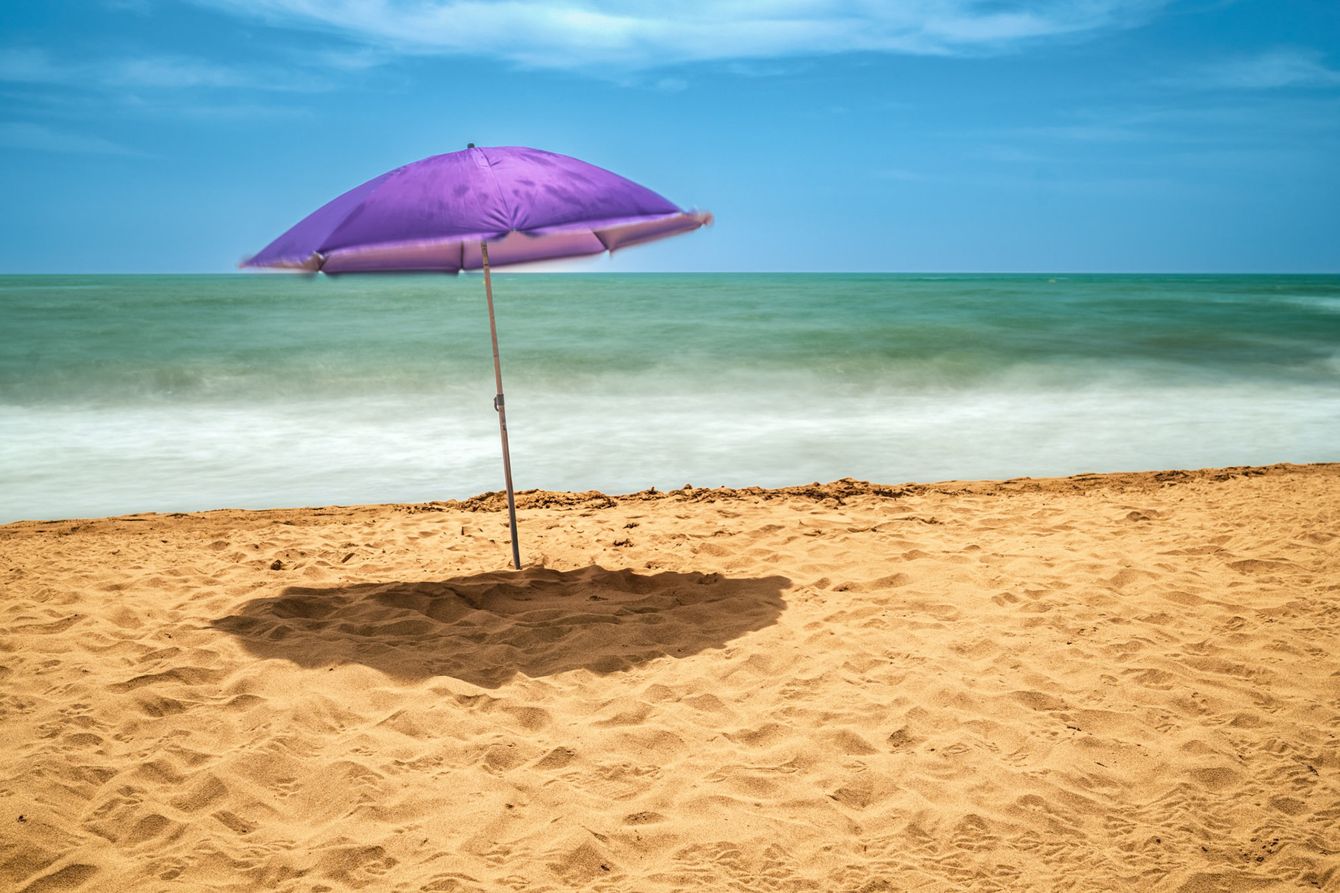 A purple umbrella alone on Isla Canela beach in Ayamonte, Spain, with gentle waves and a serene atmosphere captured in long exposure.