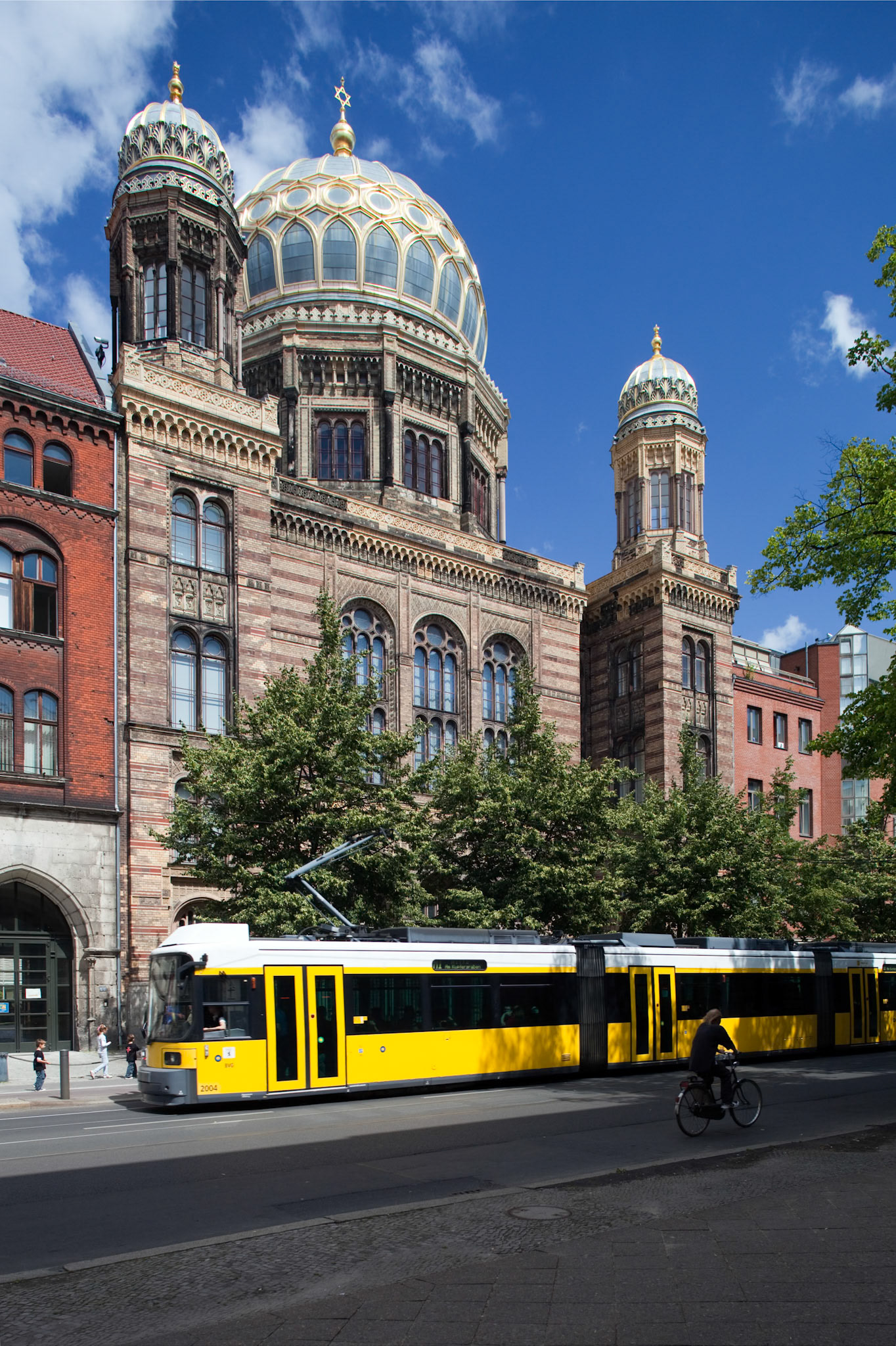 The New Synagogue in Berlin displays its ornate cupola and intricate facade, while a tram glides by the bustling street.