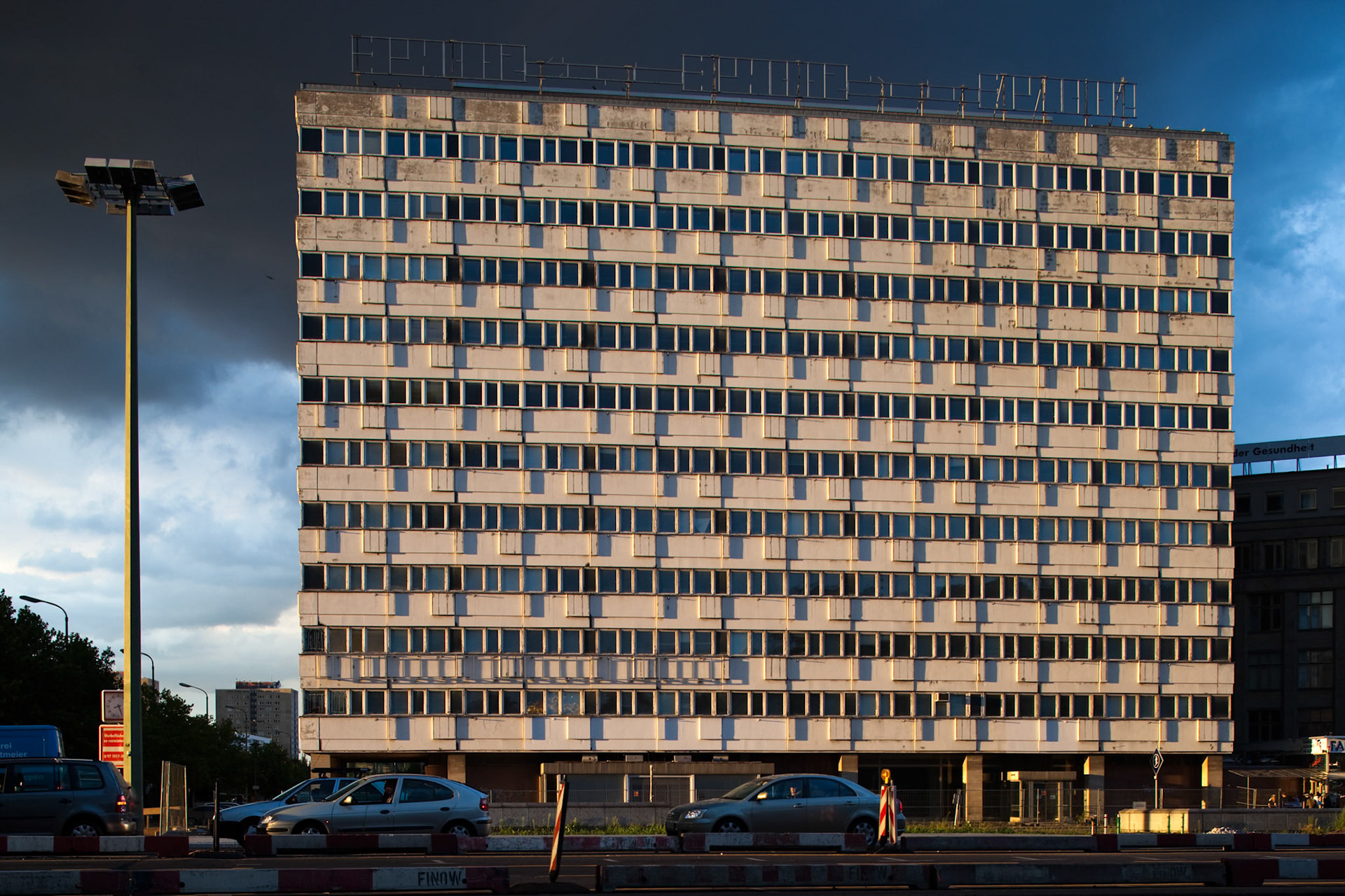 The distinctive apartment building reflects East Berlin\'s architectural style under dramatic skies.